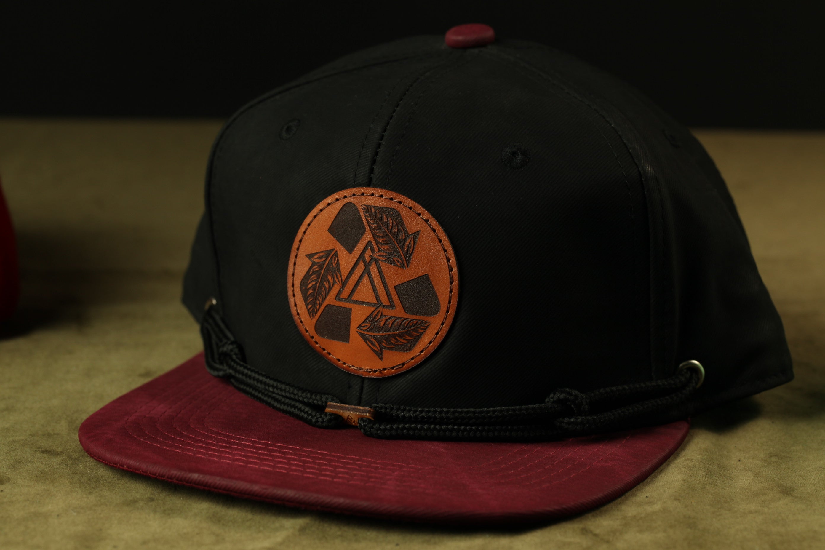 A black baseball cap with a red brim and a circular logo on the front, placed on a brown surface.