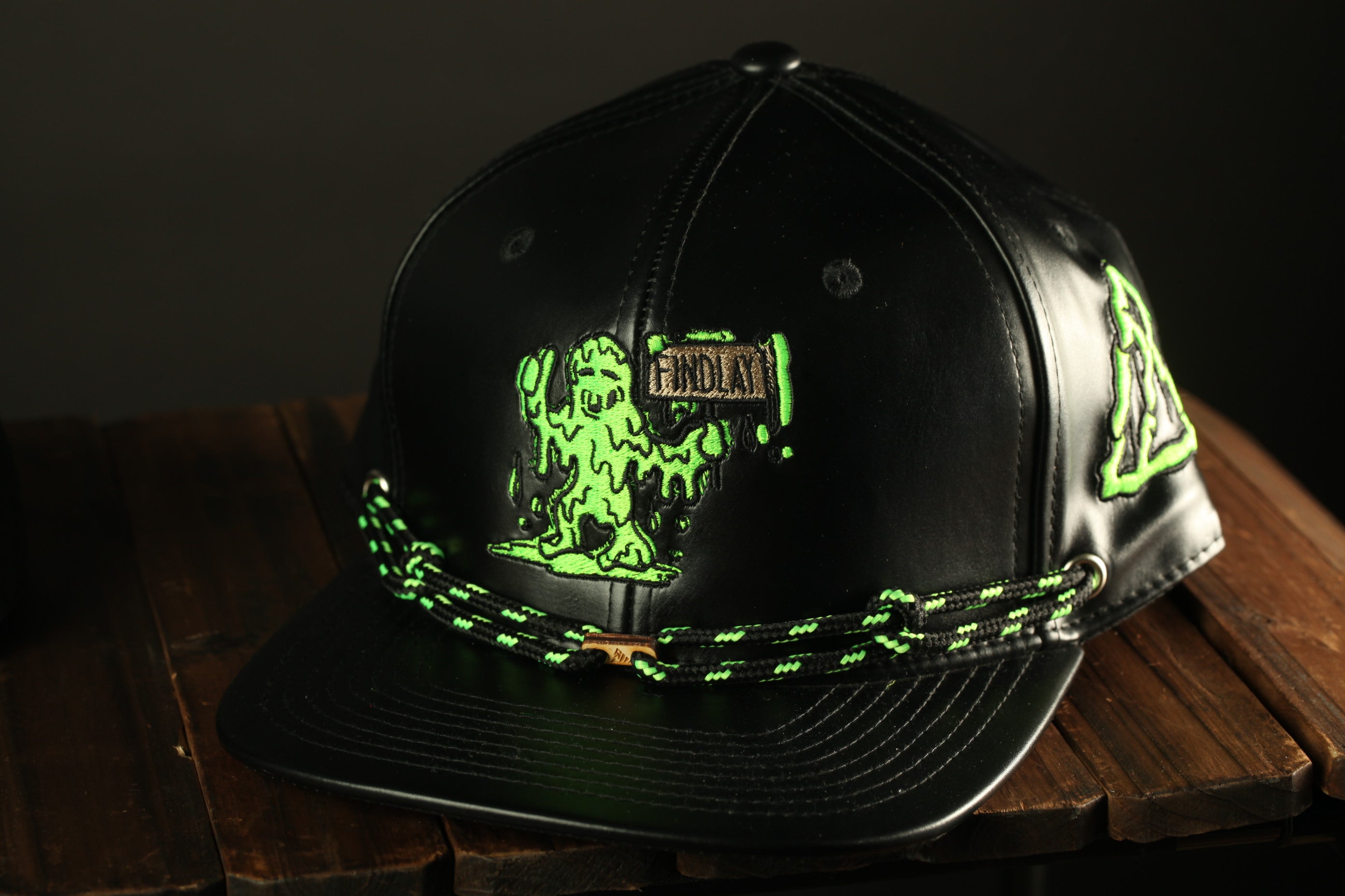 A black baseball cap with a green and black design featuring a character resembling a slimy creature.