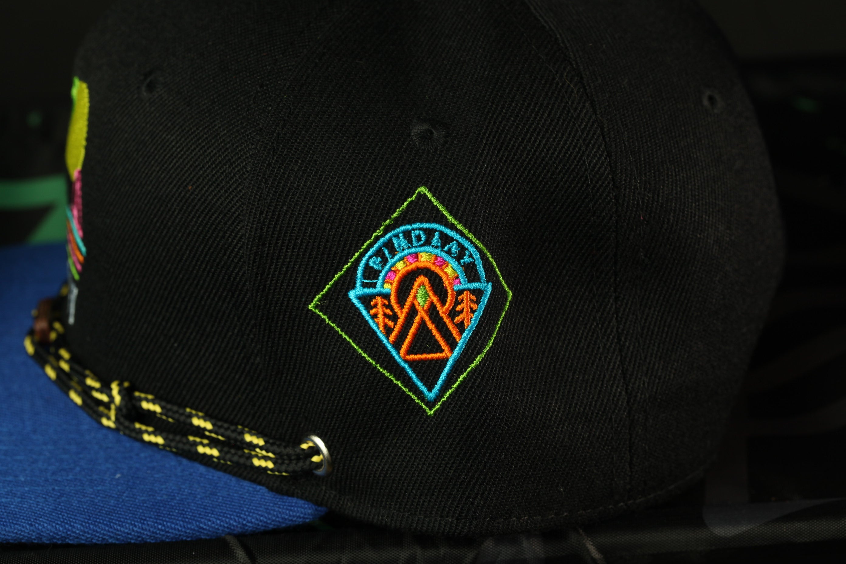 A close-up view of a black baseball cap with a colorful, embroidered logo on the front.