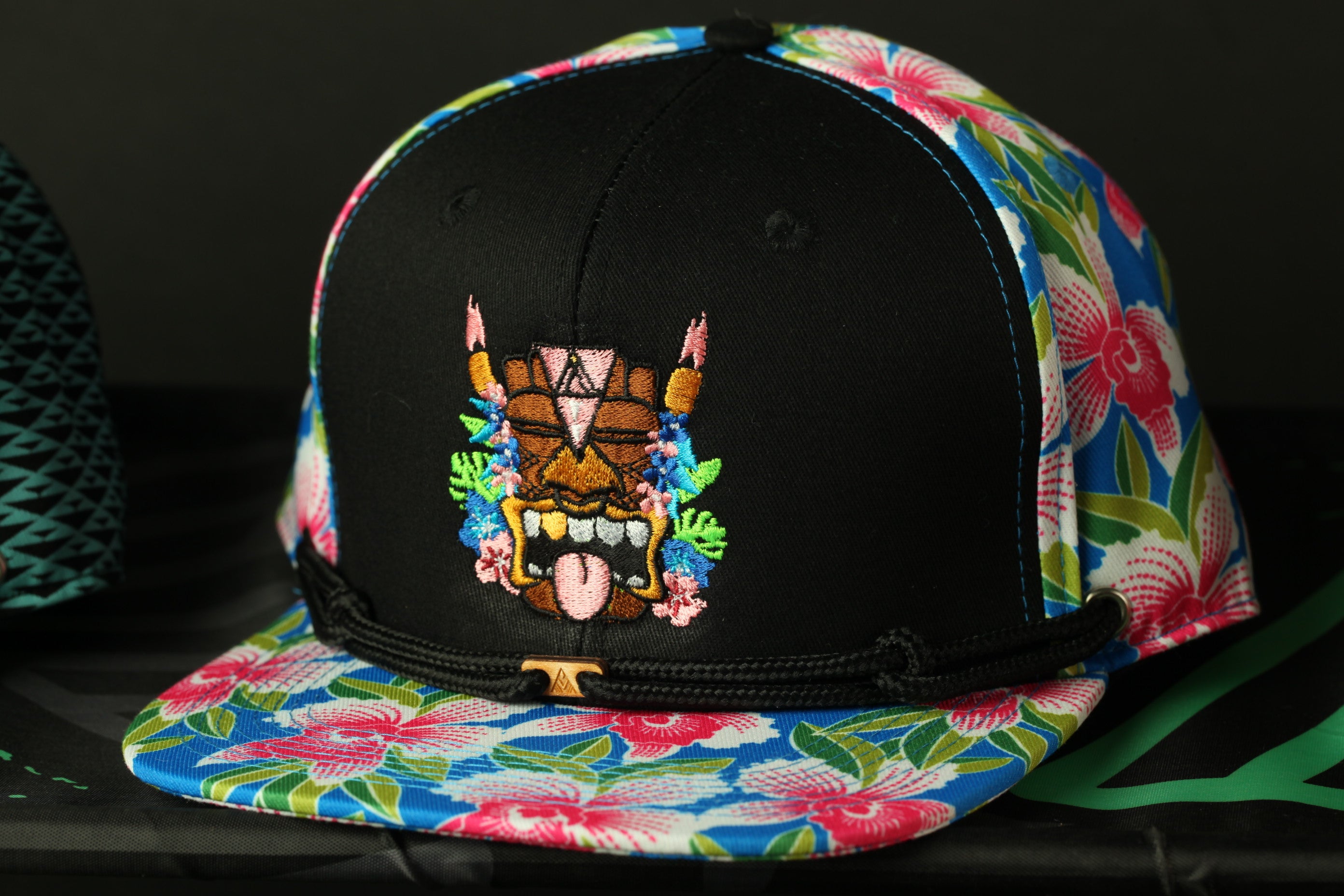 A colorful baseball cap with a floral pattern and a tiki mask design on the front.