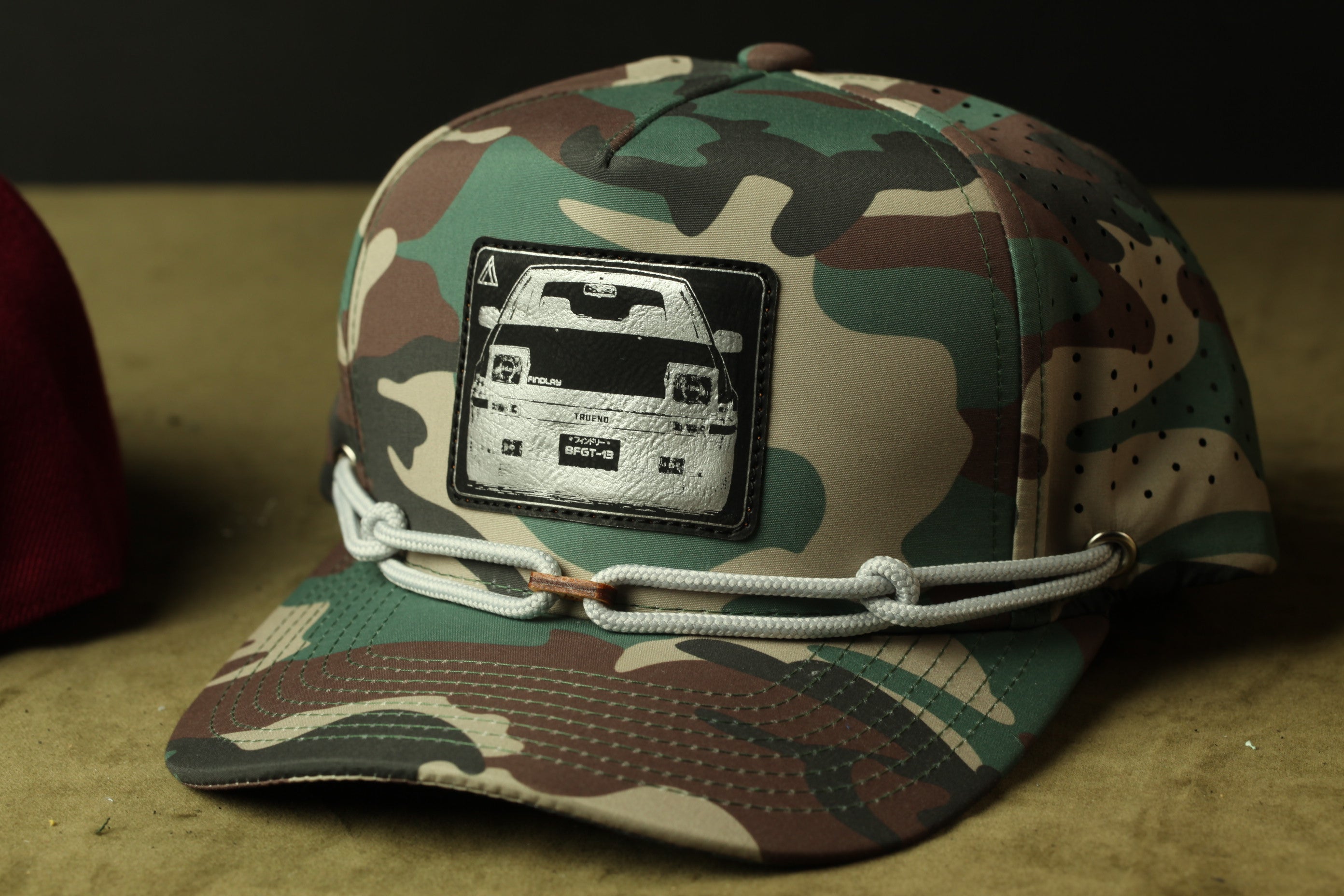 A camouflage baseball cap with a patch featuring a vehicle design.