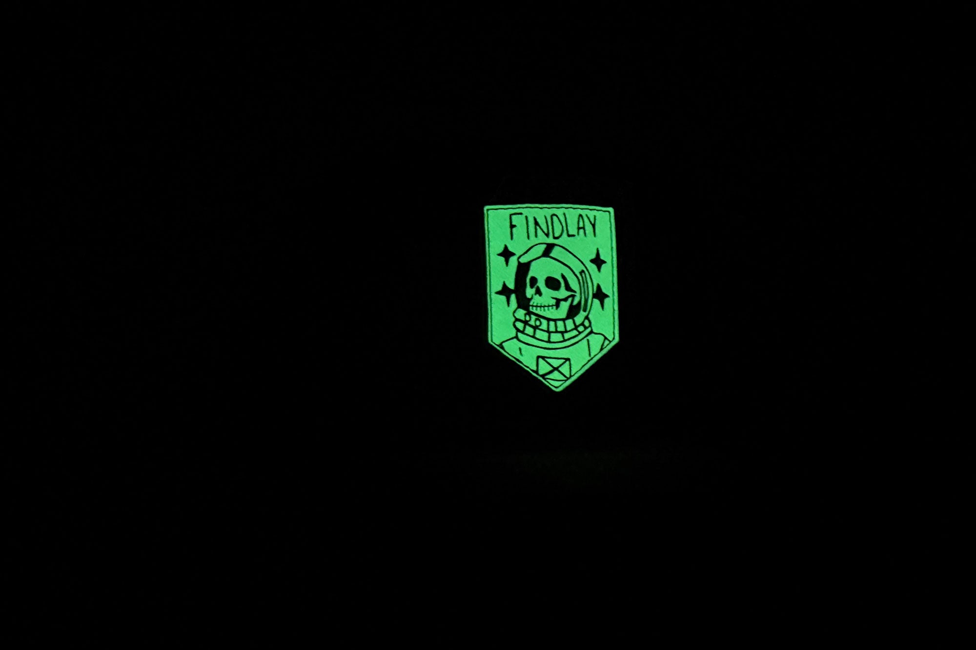 A green patch with a skull and the word "FINDLAY" illuminated against a black background.