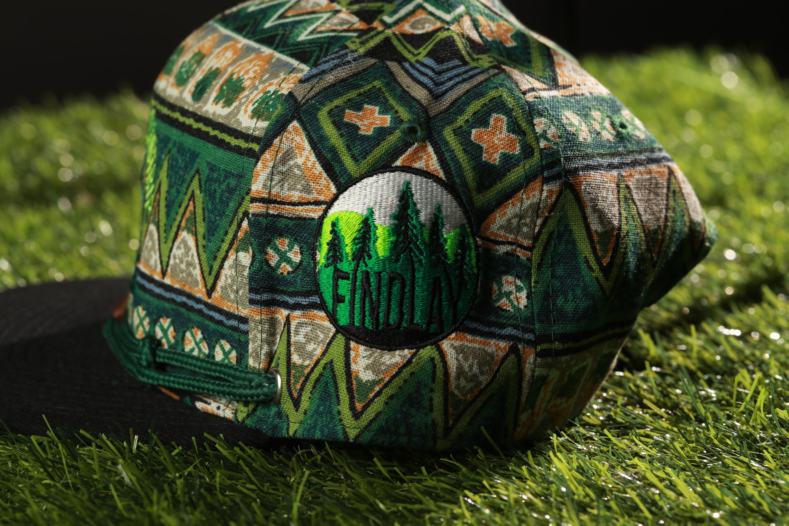 A colorful, patterned baseball cap with a green and orange design, featuring a central circular patch with the word "FINDlay" printed on it.