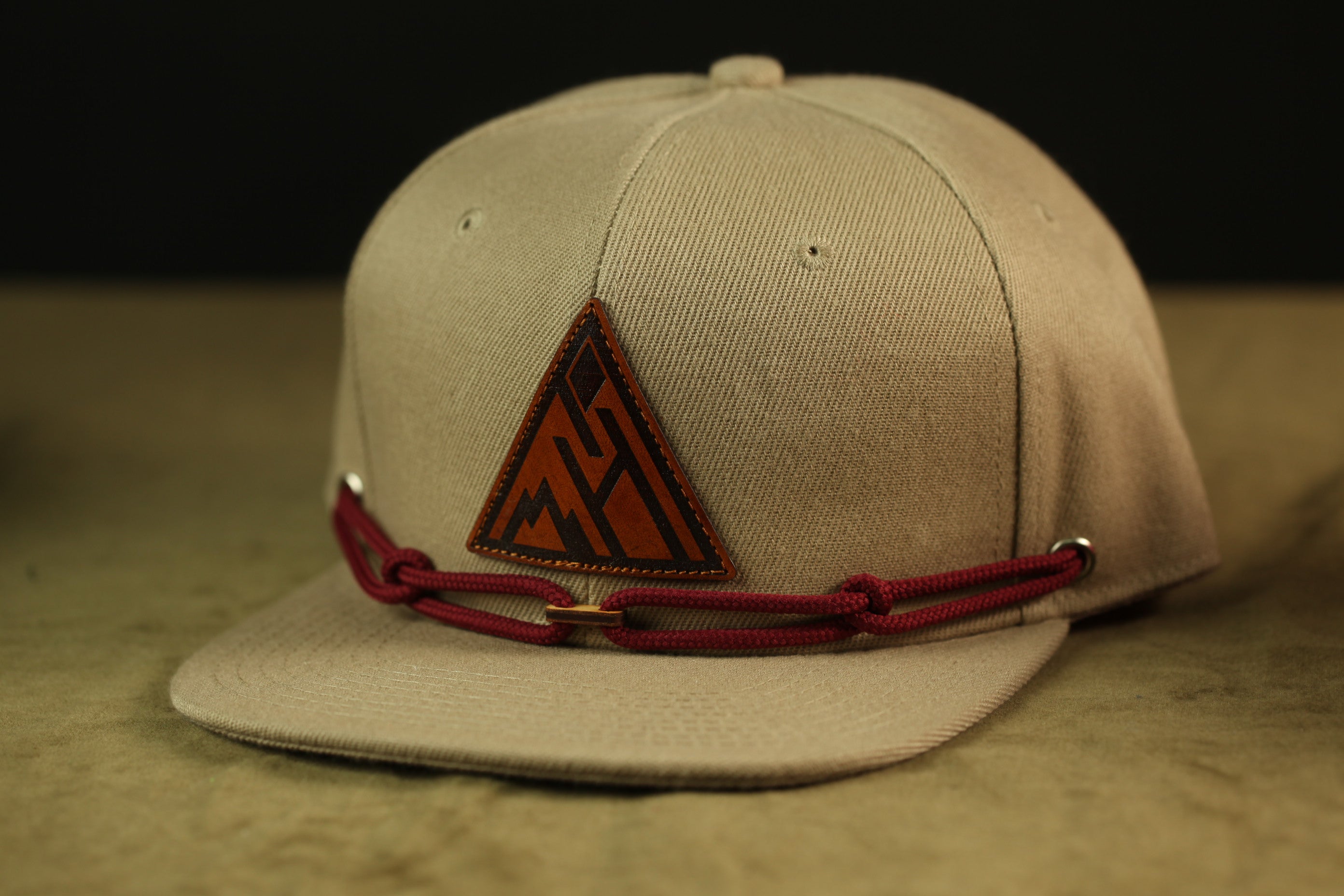 A beige baseball cap with a red leather patch and a red string or chain attached to it.