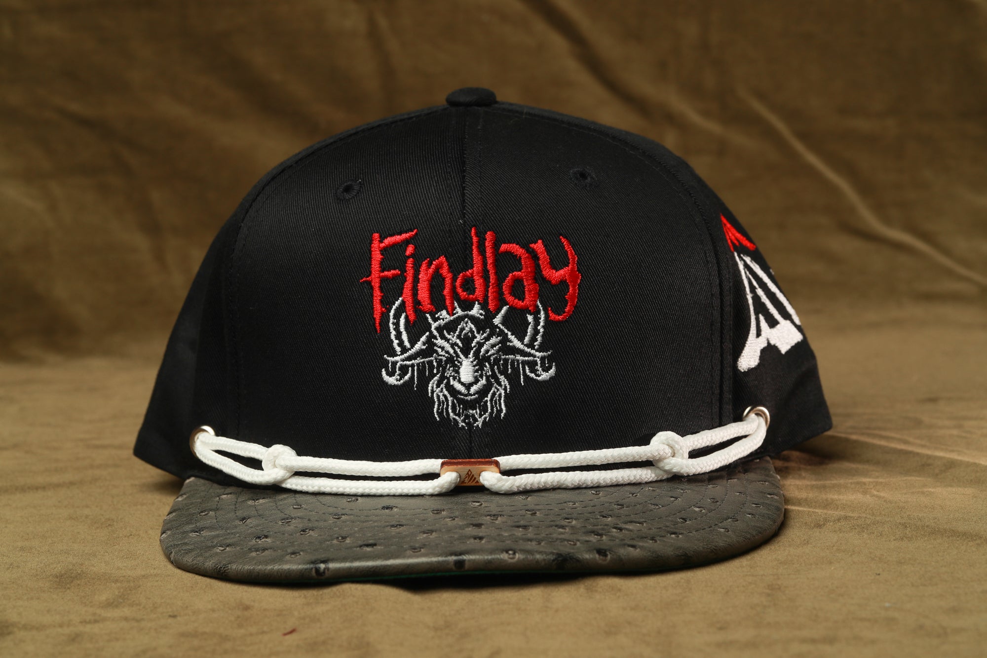 A black baseball cap with a red and white logo on the front, featuring a goat or ram design.
