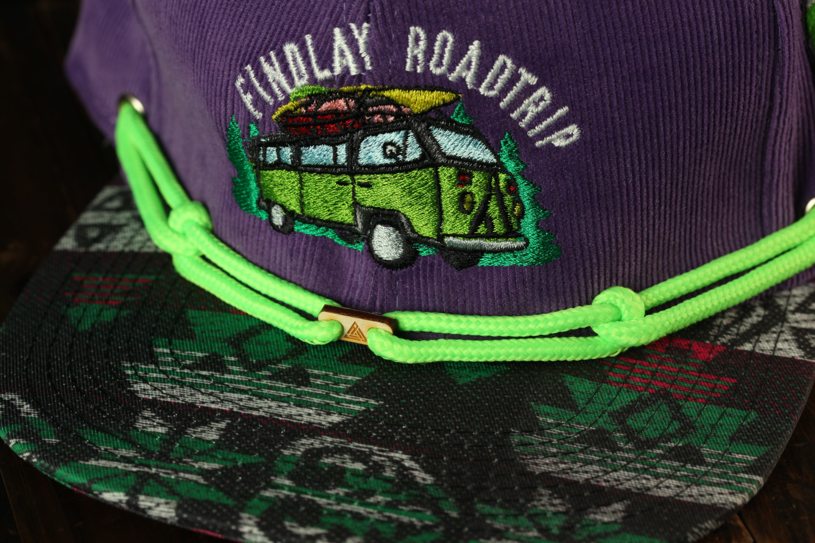 A purple baseball cap with a green string and a graphic of a van on it.