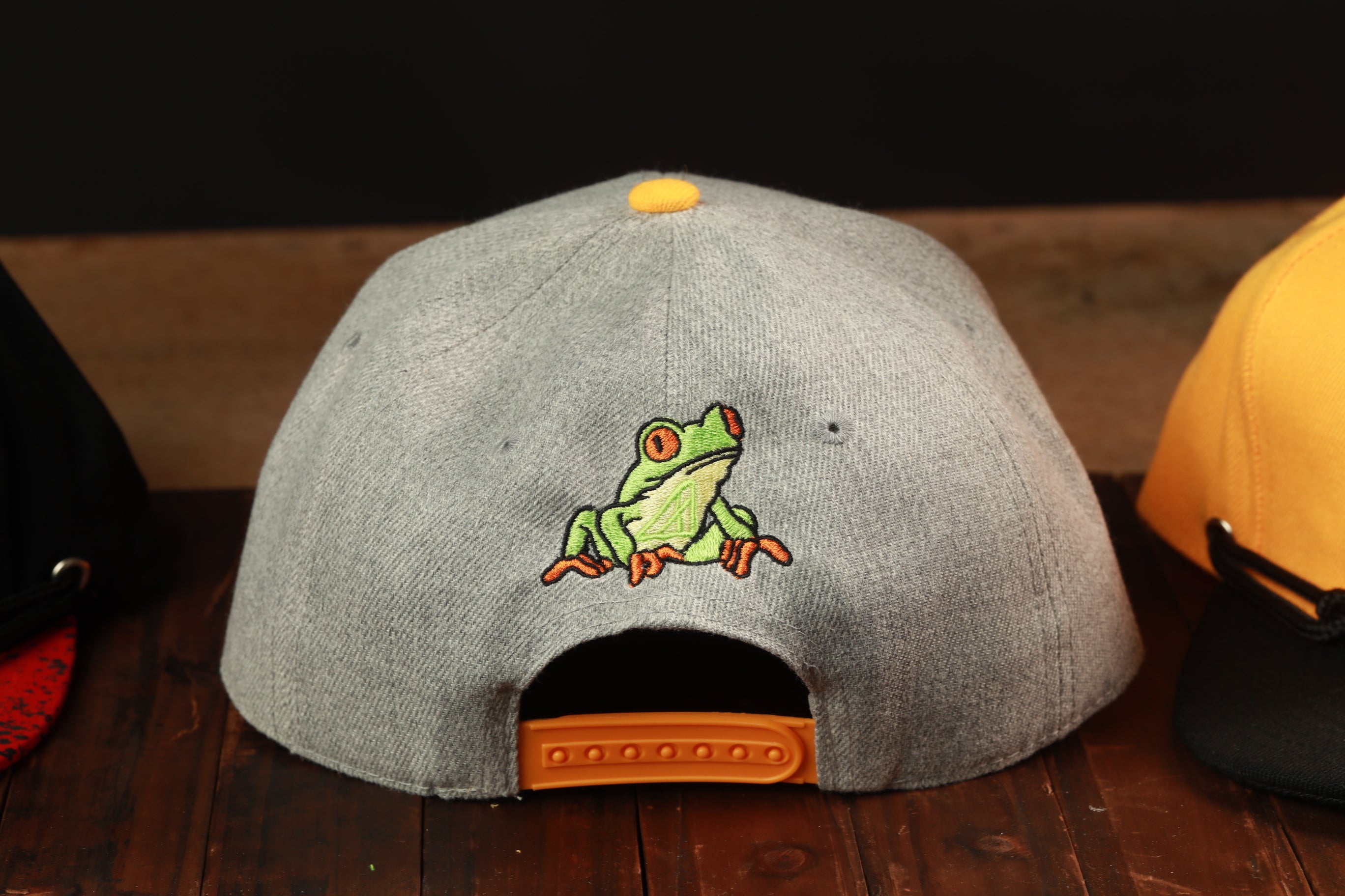A gray baseball cap with a green frog embroidered on it, sitting on a wooden surface.
