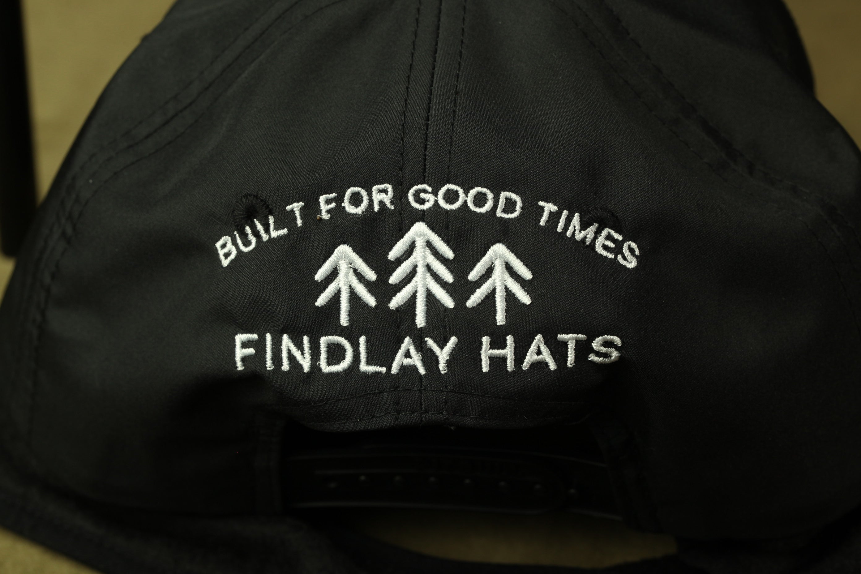 the back of a black baseball cap with white text and three tree silhouettes embroidered on it.