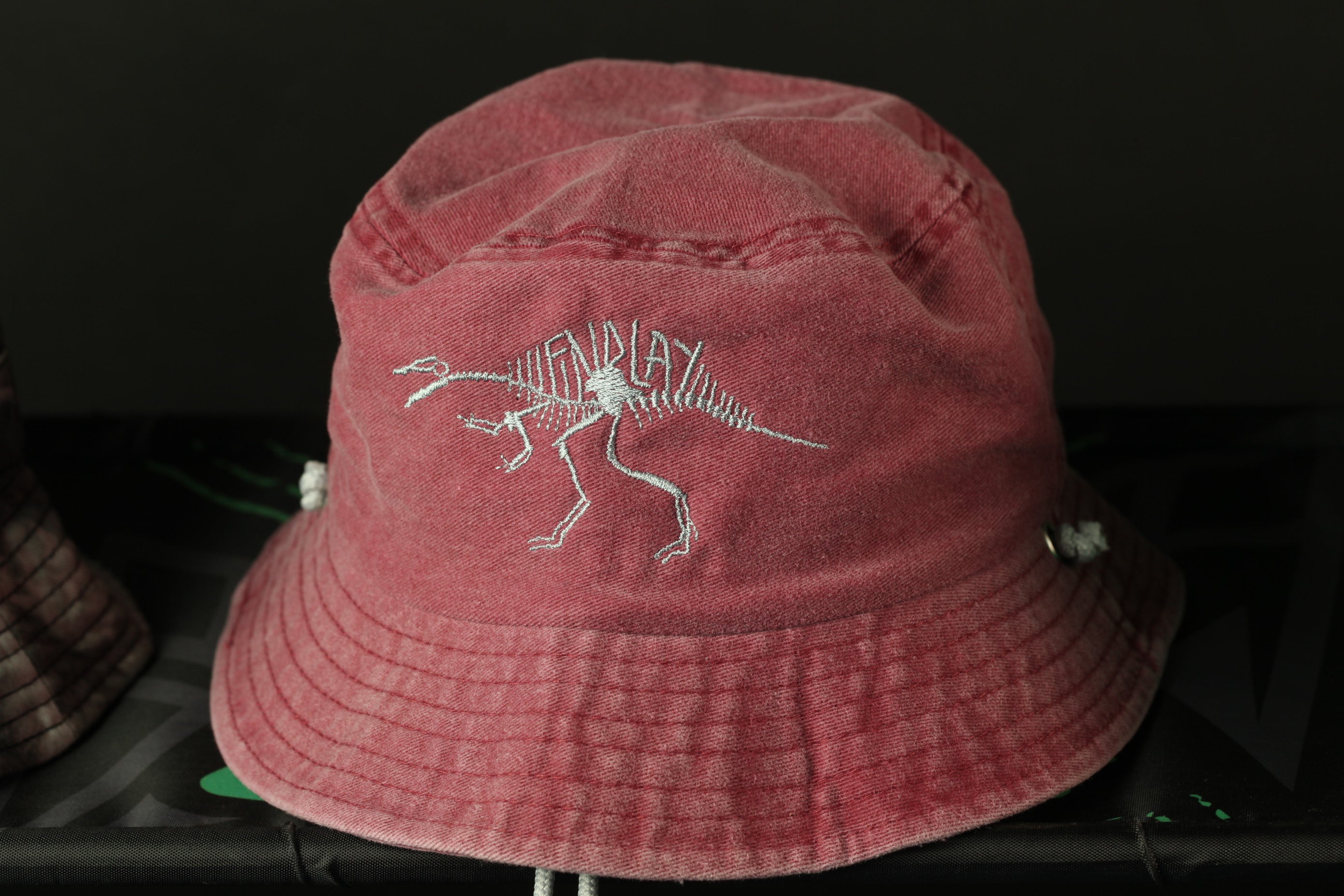 A red bucket hat with a dinosaur skeleton embroidered on it.