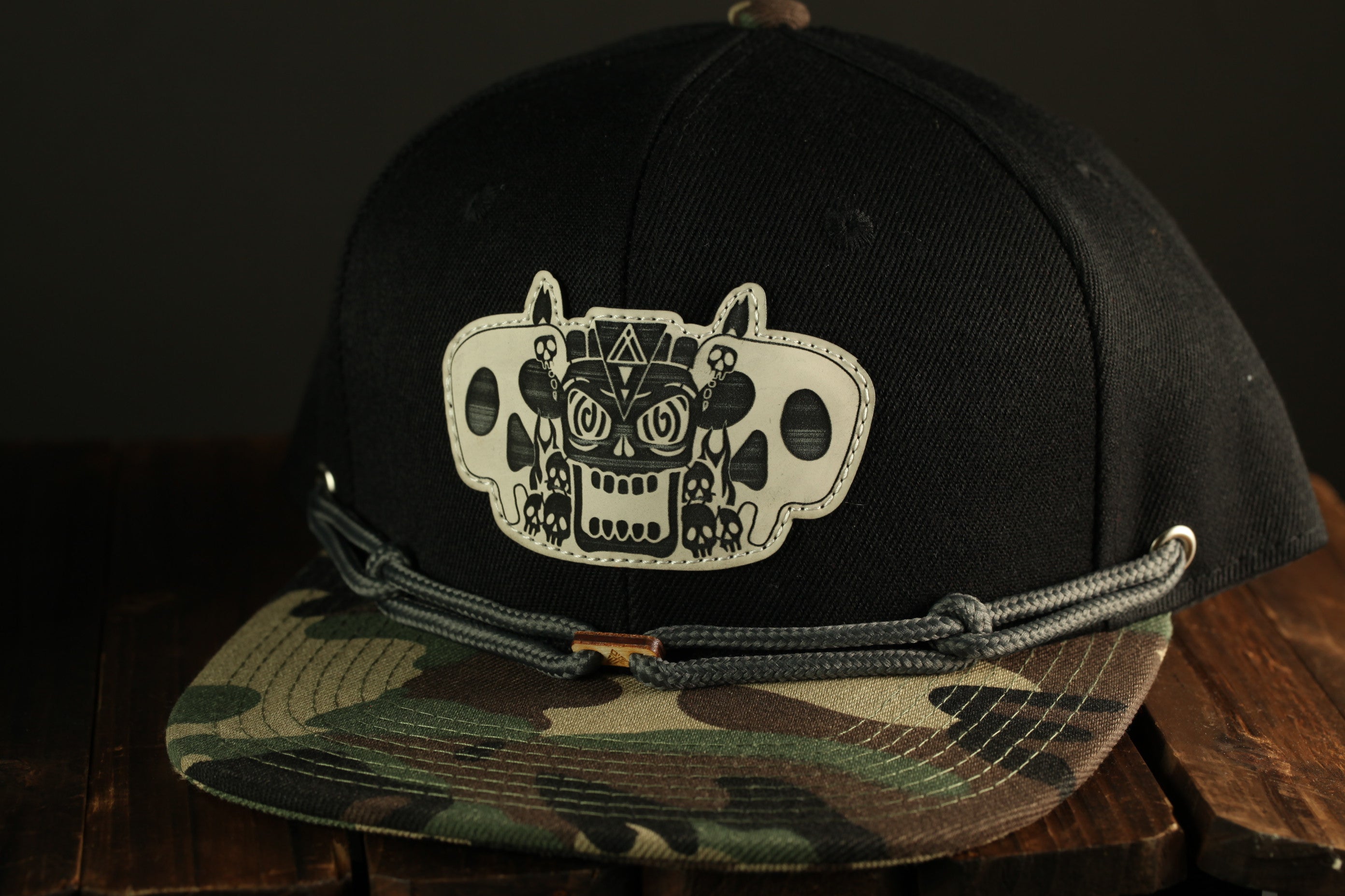 A black baseball cap with a white skull design on the front, placed on a wooden surface.