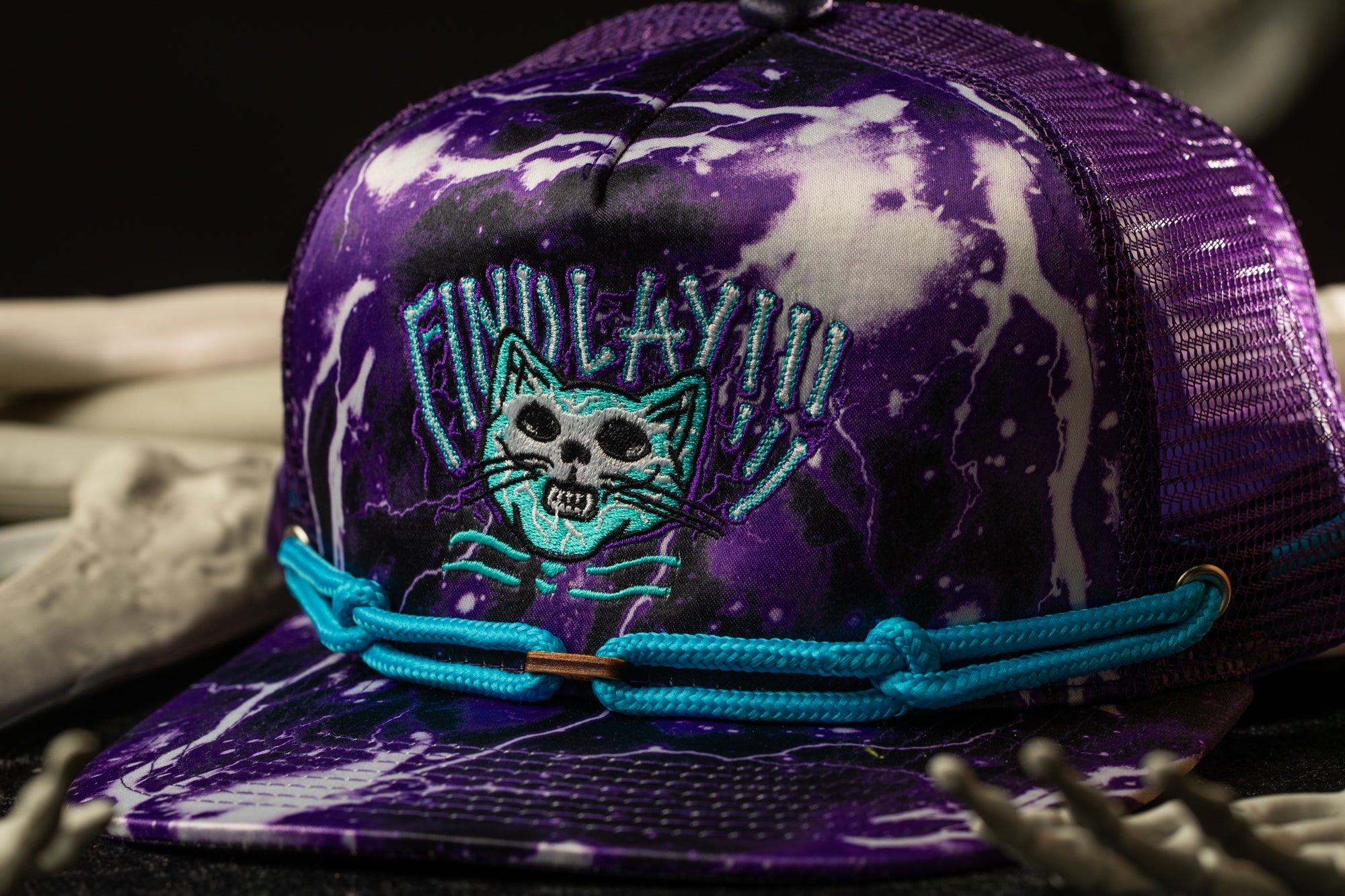 A purple baseball cap with a cat design and a blue strap.
