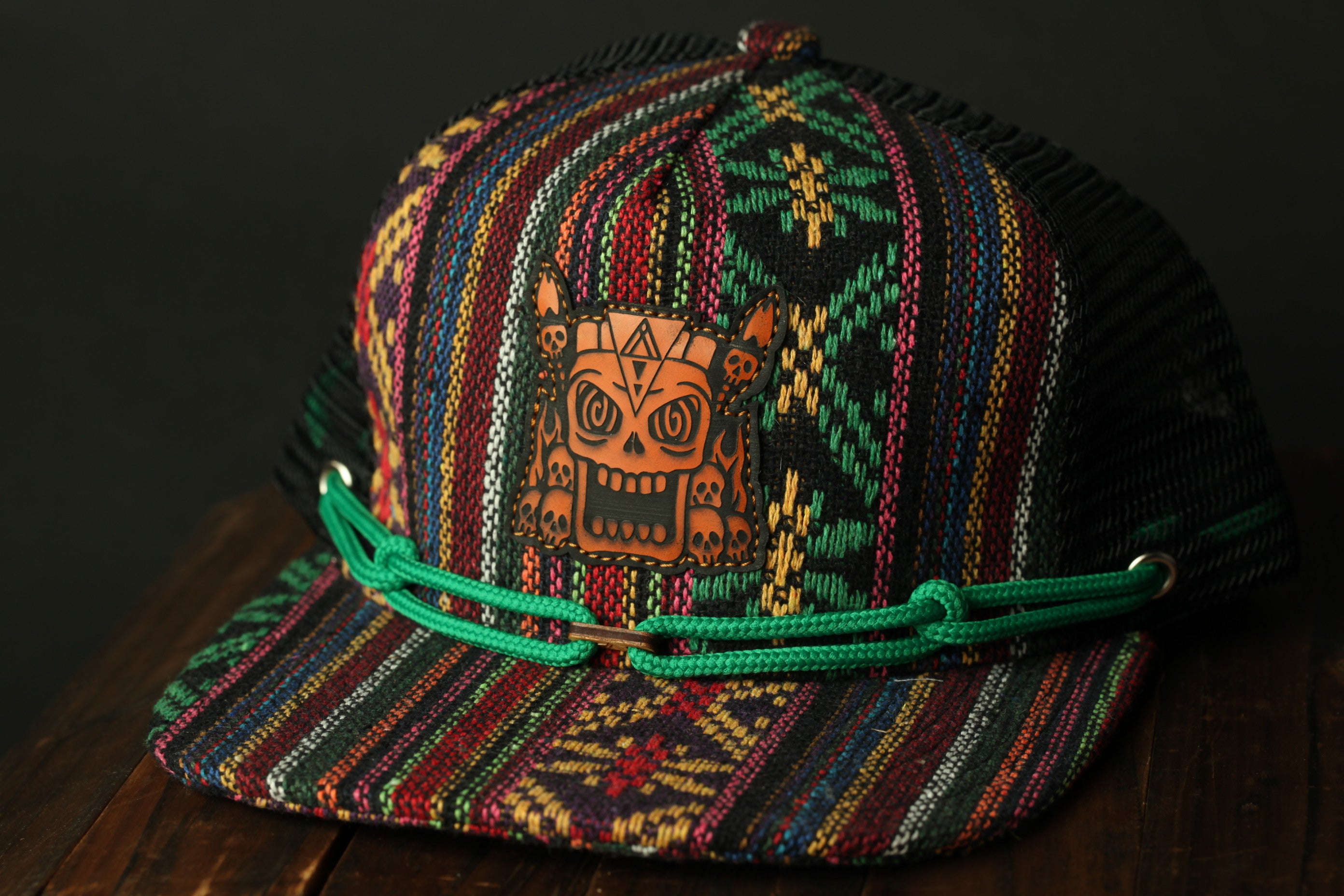 A colorful, patterned baseball cap with a skull design on the front, sitting on a wooden surface.