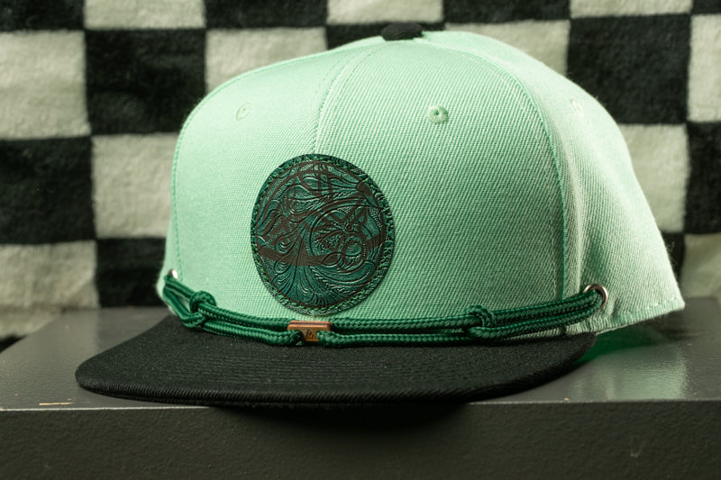 A mint green baseball cap with a black brim and a circular logo on the front, displayed against a black and white checkered background.