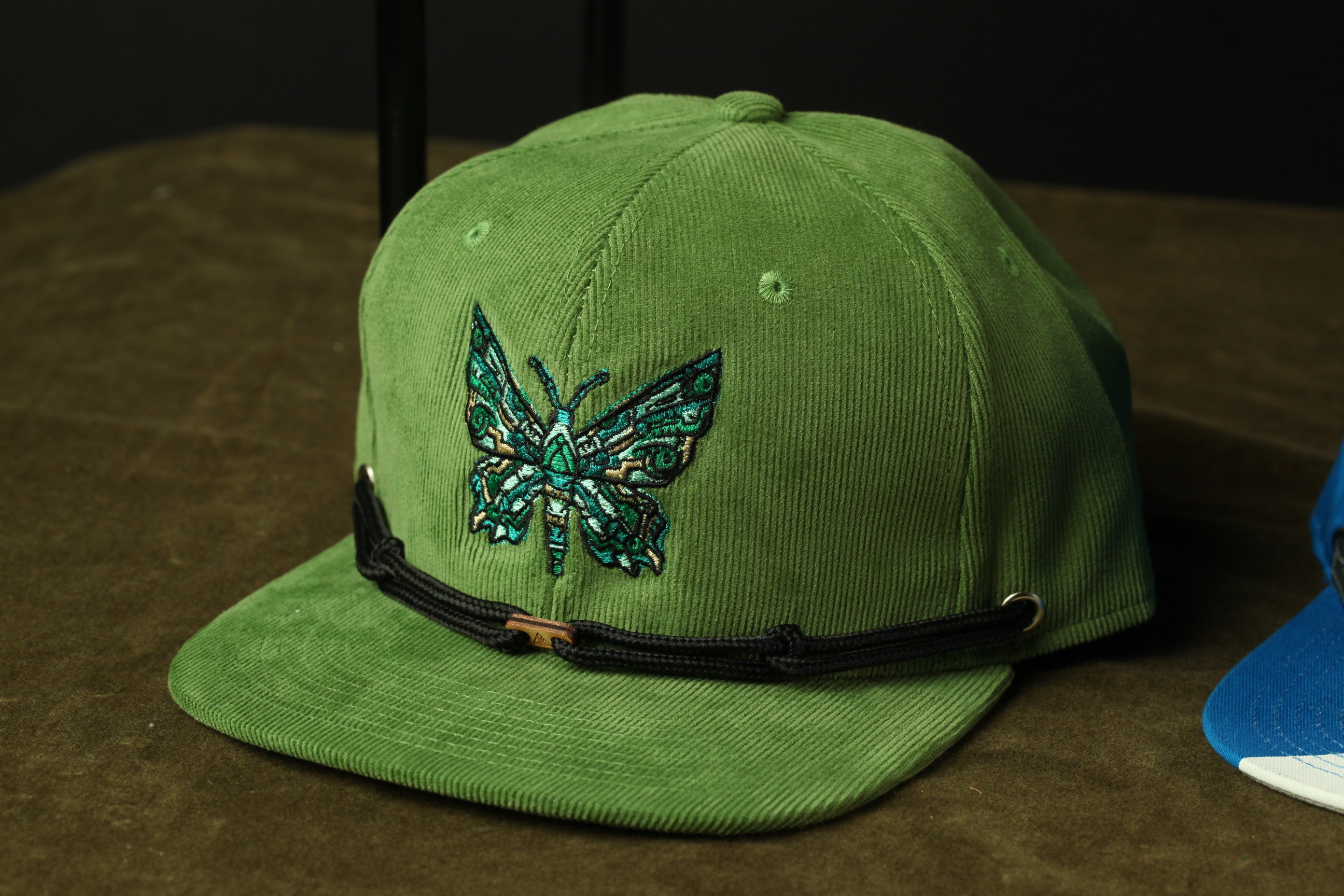 A green baseball cap with a butterfly embroidered on it, placed on a brown surface.