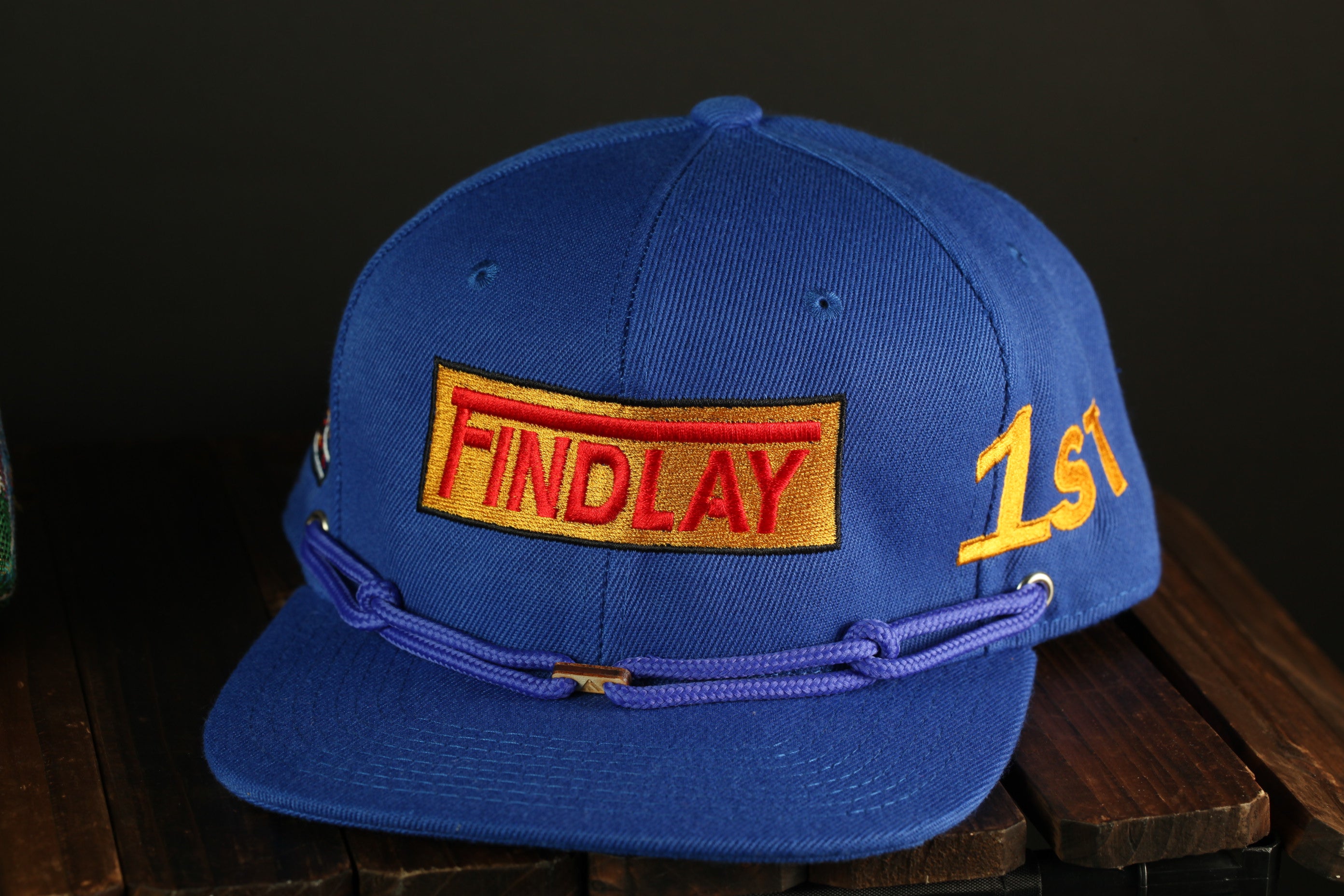 A blue baseball cap with a red and gold embroidered logo on the front, sitting on a wooden surface.