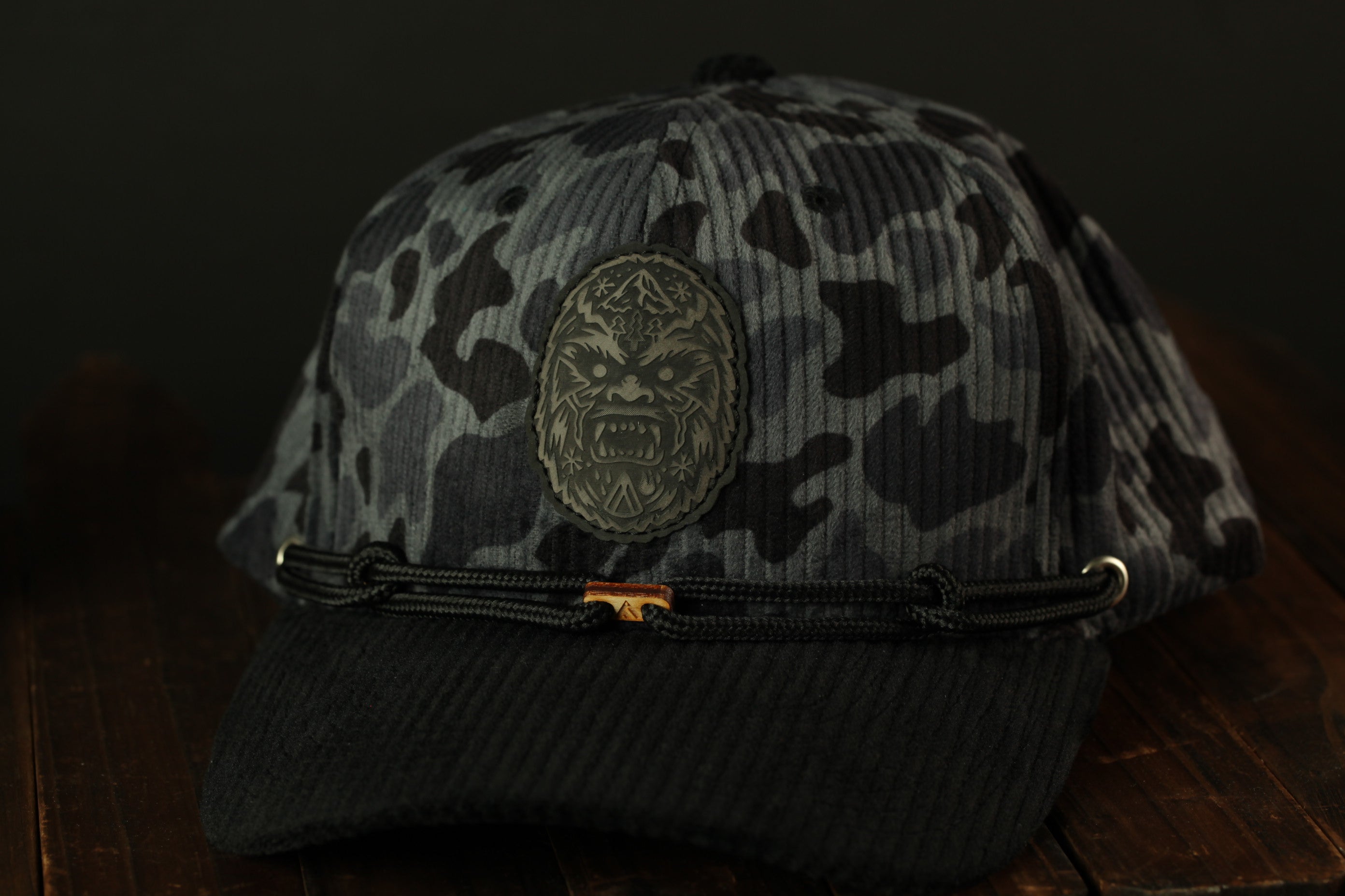 A black and gray camouflage baseball cap with a distinctive logo on the front.