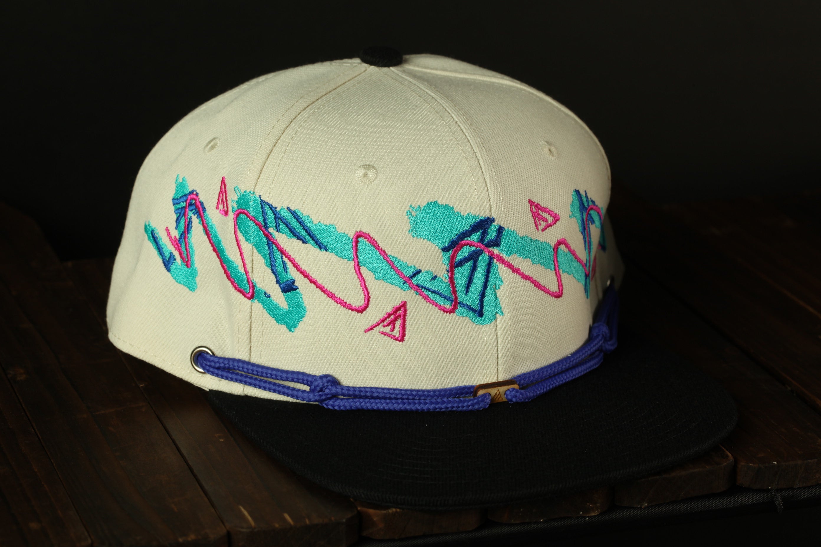 A white baseball cap with colorful embroidered designs on the front, sitting on a wooden surface.