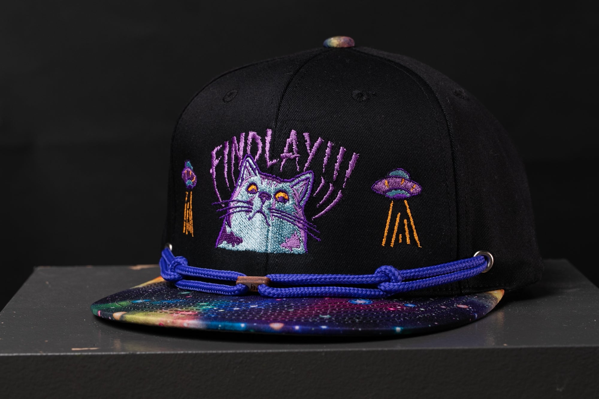 A black baseball cap with a colorful, space-themed design and embroidered cat graphics.