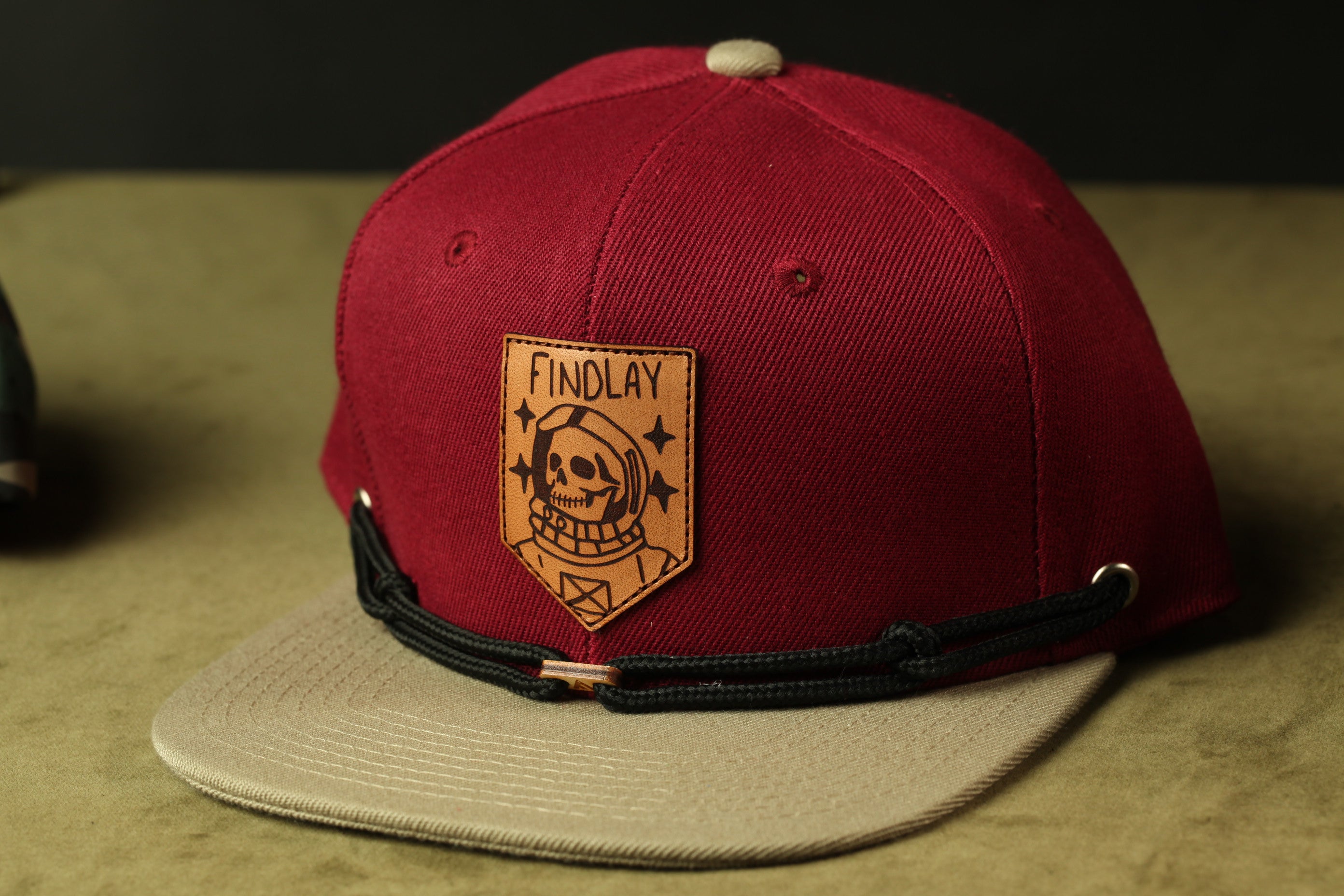 A red baseball cap with a black strap and a patch featuring a skull and the word "FINDLAY" printed on it.