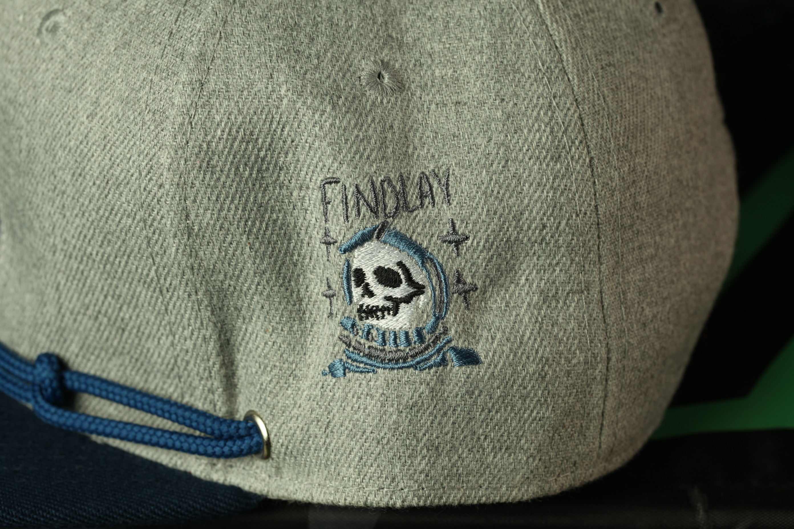 a gray baseball cap with a blue string and a small embroidered design on the front.