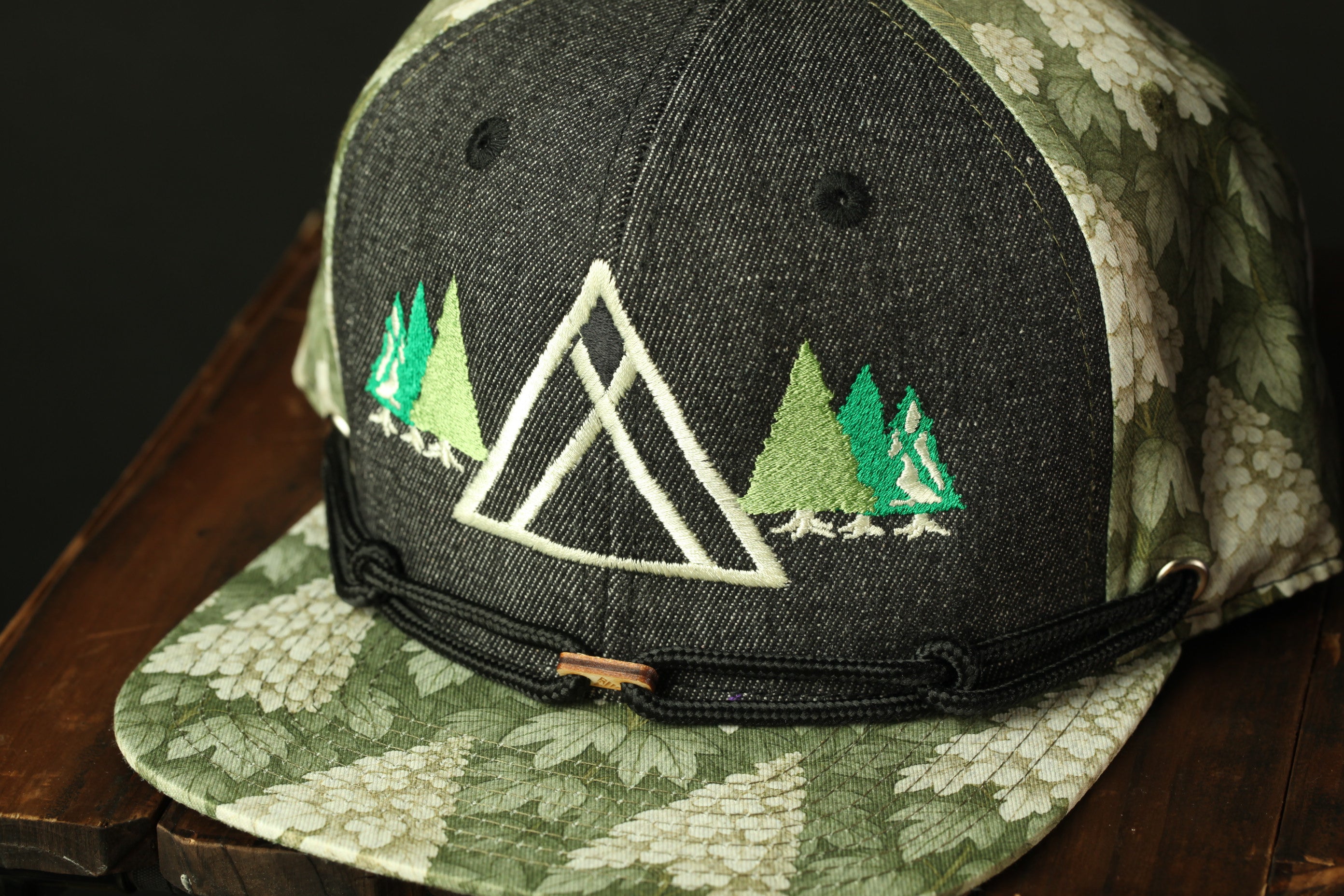 A black baseball cap with a green and white floral pattern and a white triangle design on the front.