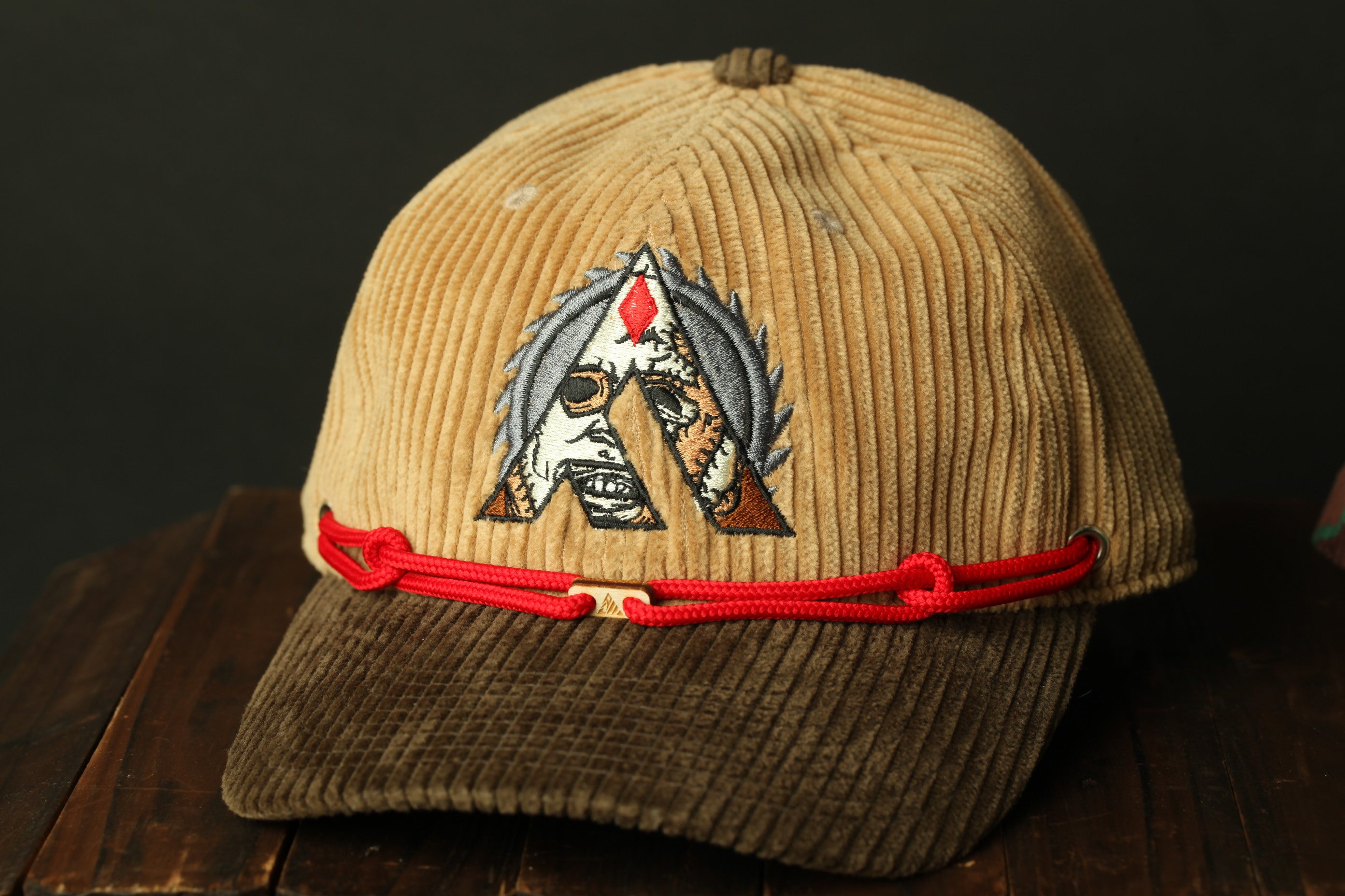 A brown baseball cap with a red string and a detailed embroidered logo on the front.
