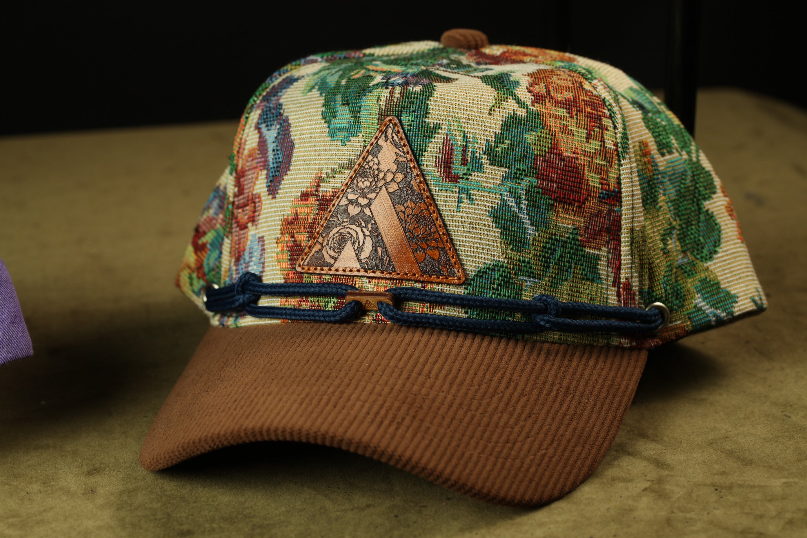 A colorful, patterned baseball cap with a floral design and a metal patch on the front.