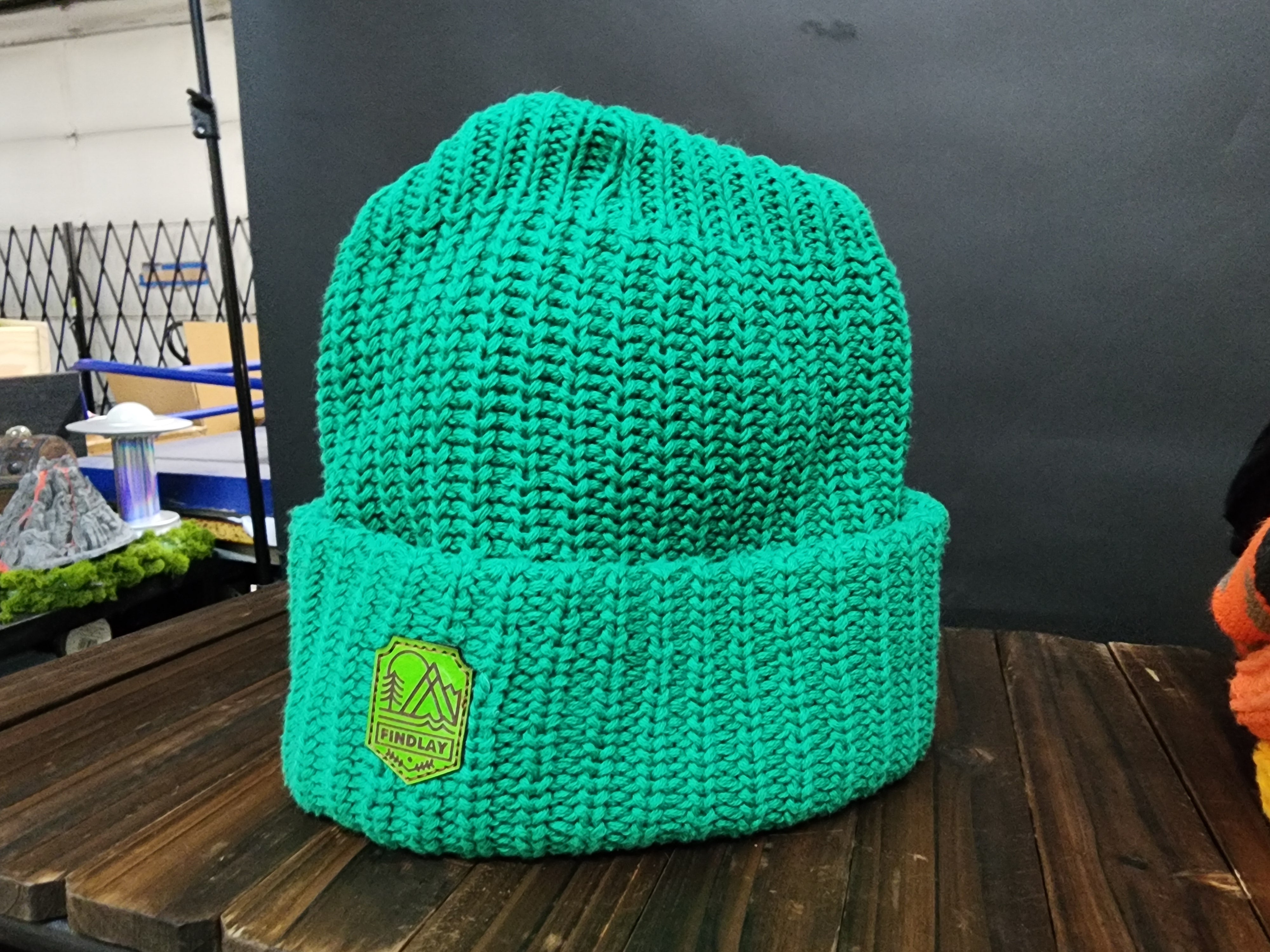 A bright green knitted beanie with a green patch on the front, sitting on a wooden surface.