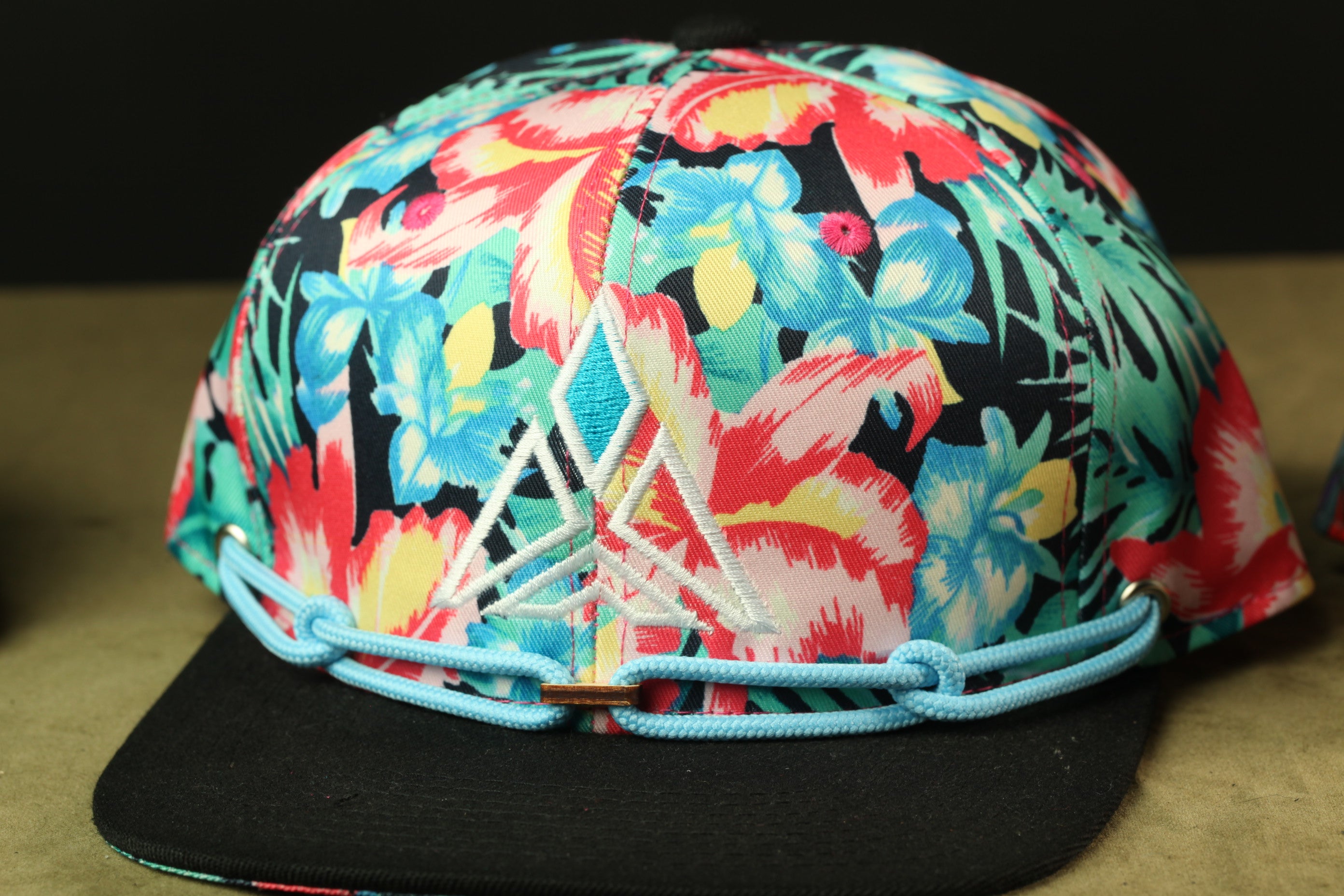 A colorful floral printed baseball cap with a black brim and blue adjustable strap.