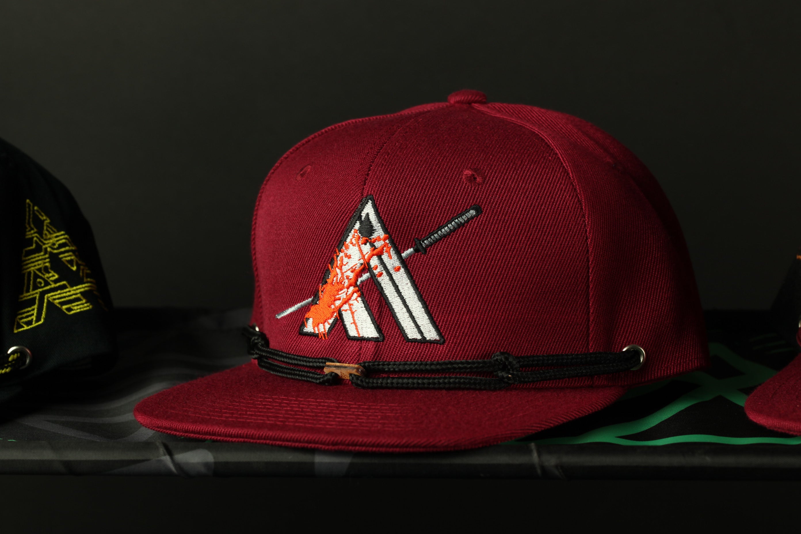 A maroon baseball cap with a graphic design on it, placed on a surface.