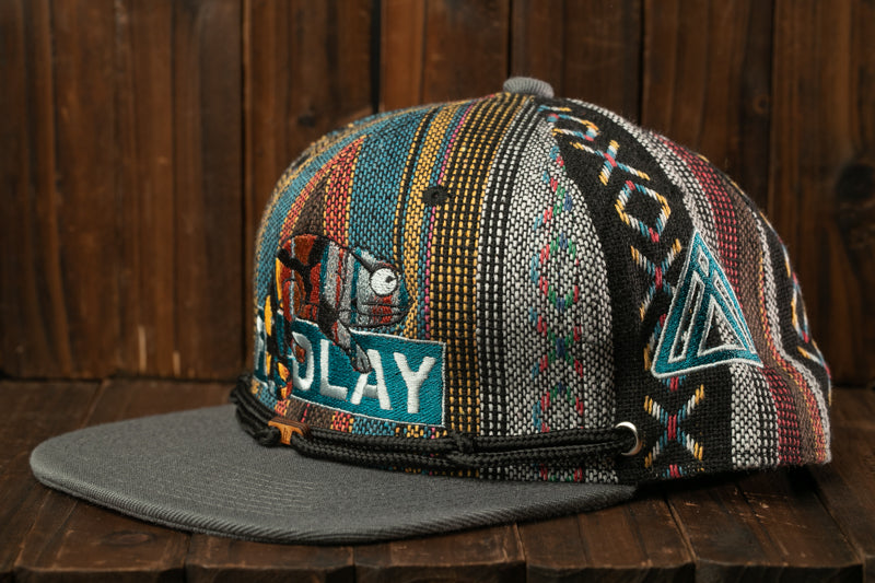 A colorful, patterned baseball cap with a gray brim and a black band, featuring a design with a fish and the word "PLAY" on it.