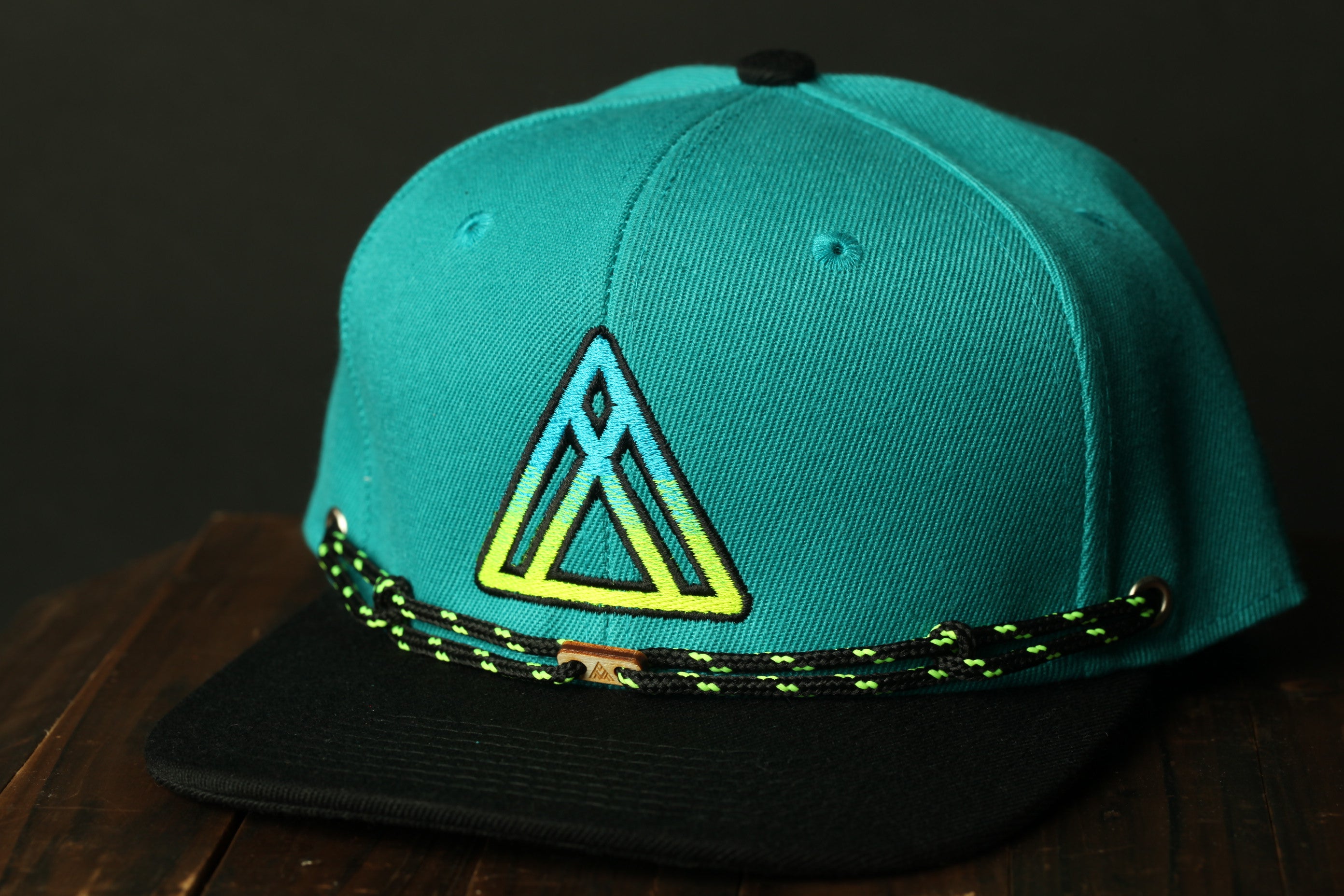 A turquoise baseball cap with a black brim and a yellow and green geometric pattern on the front.