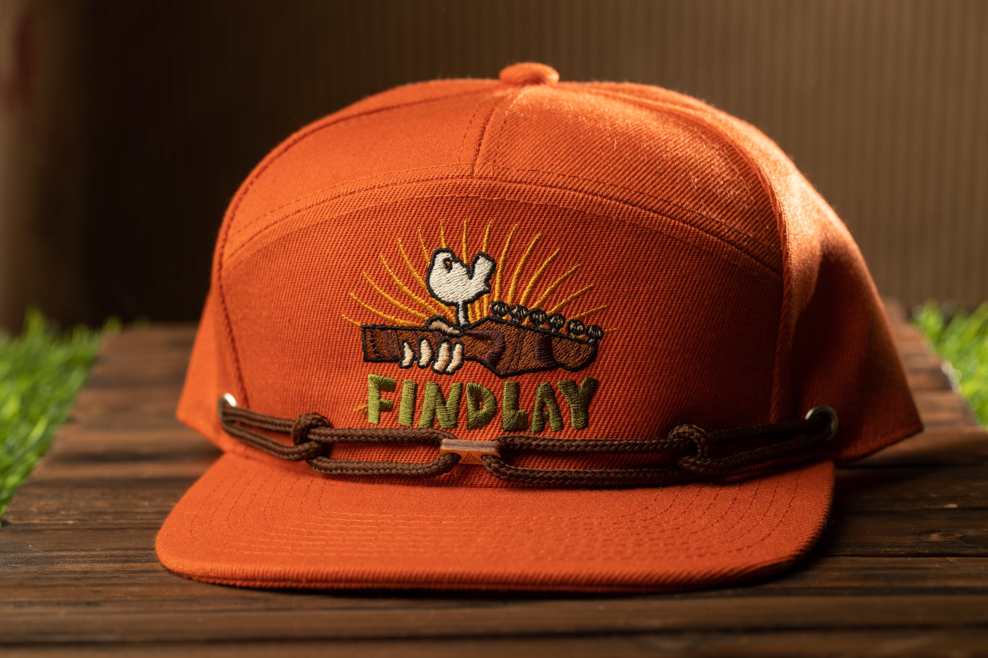 An orange baseball cap with a cartoon image of a bird holding a guitar and the text "FINDPLAY" printed on it.