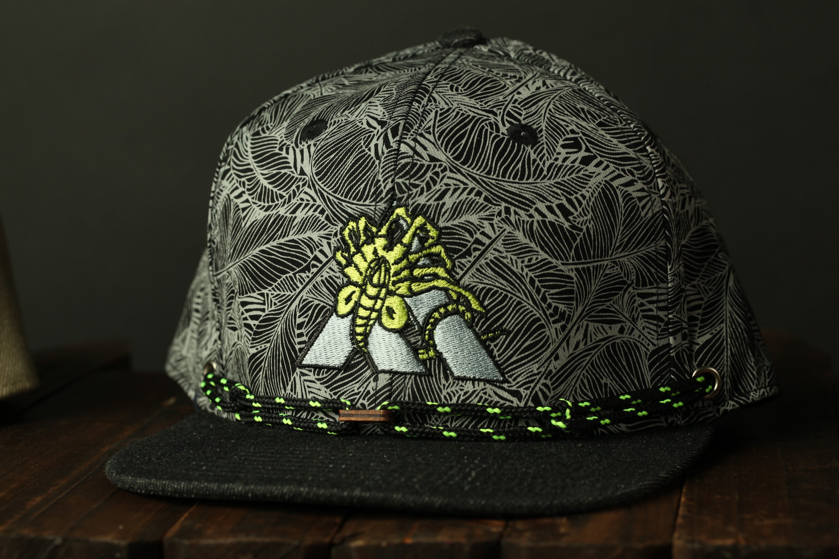 A black and gray patterned baseball cap with a yellow and black design on the front, sitting on a wooden surface.