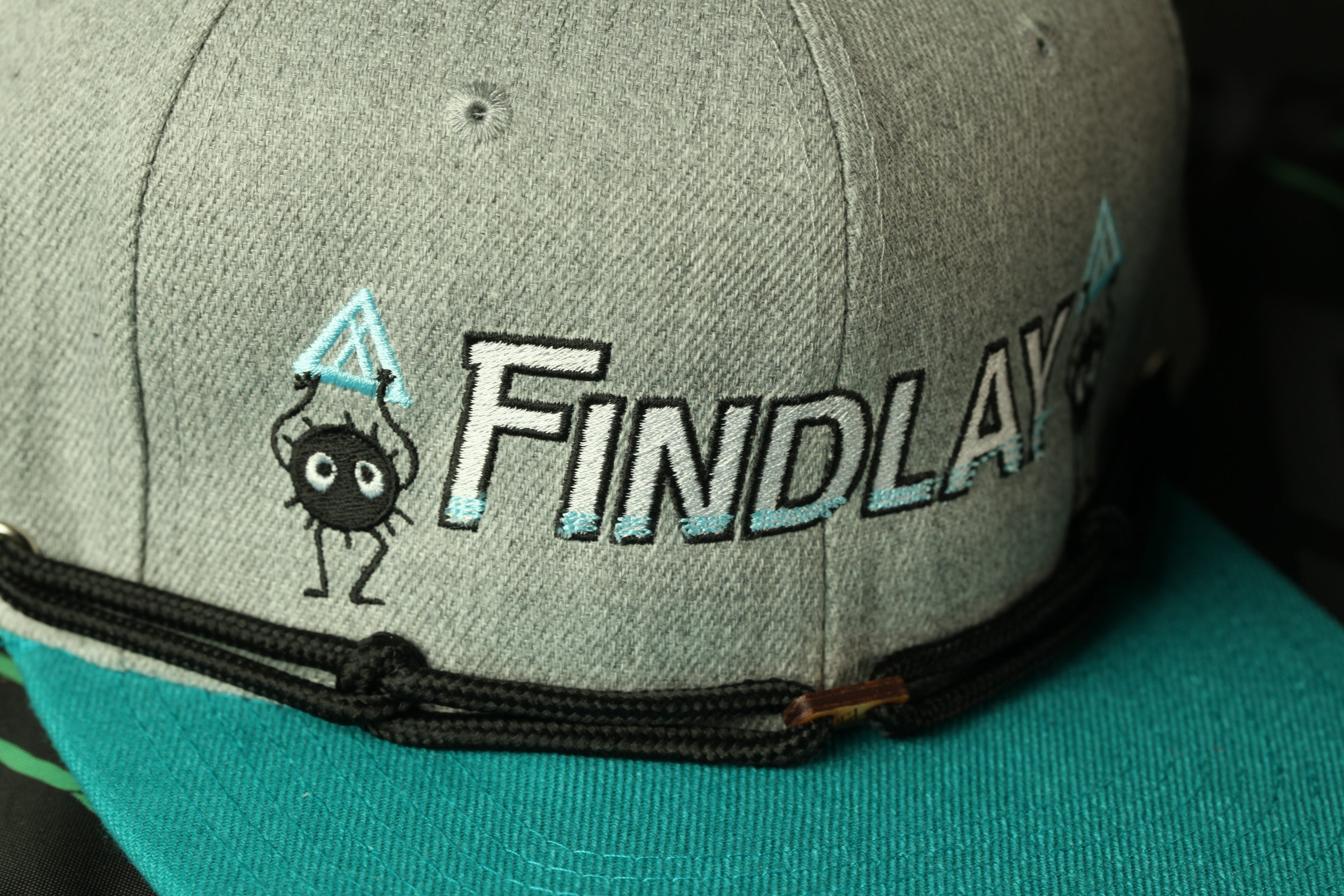 A gray baseball cap with the word "Findlay" embroidered on it, along with a small cartoon character holding a triangle.