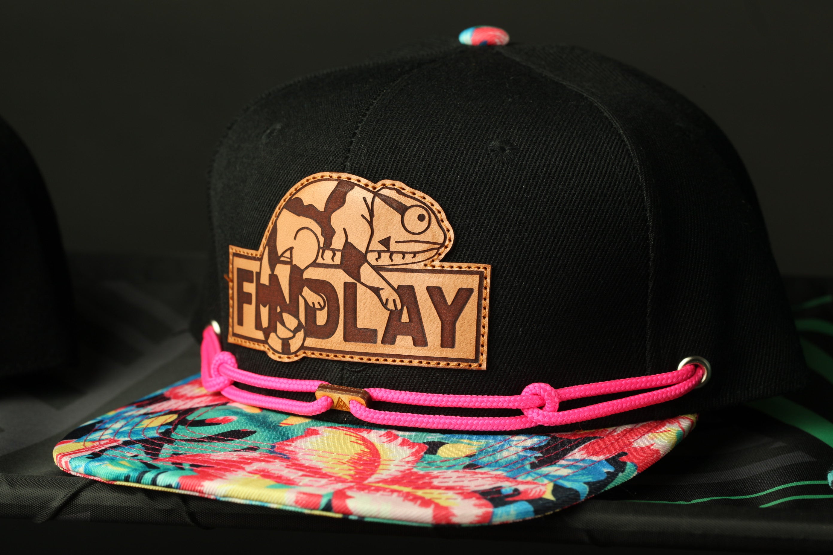 A black baseball cap with a colorful floral pattern and a patch featuring a cartoon character.