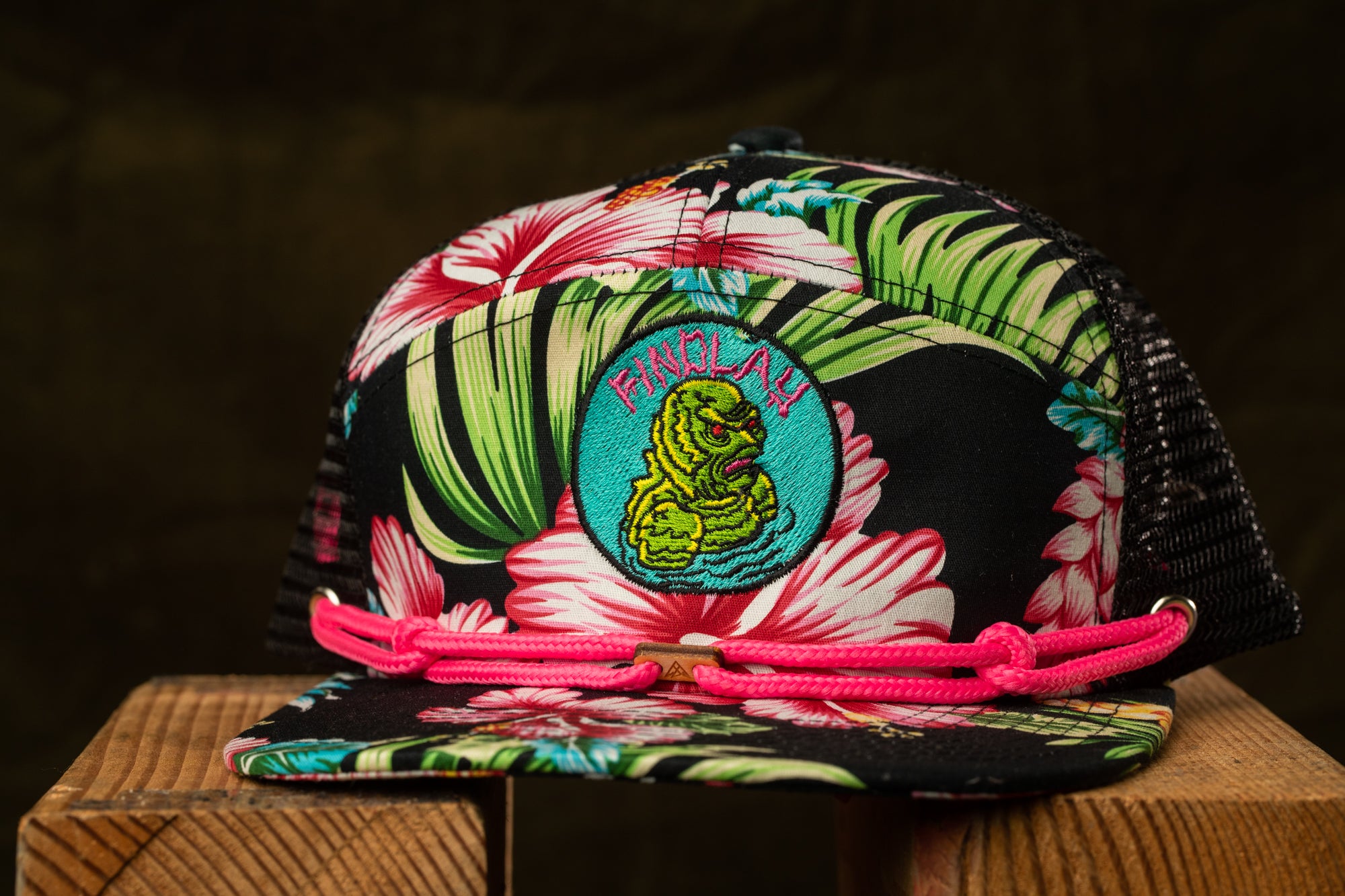 A colorful floral-patterned baseball cap with a pink braided strap and a small embroidered logo on the front.