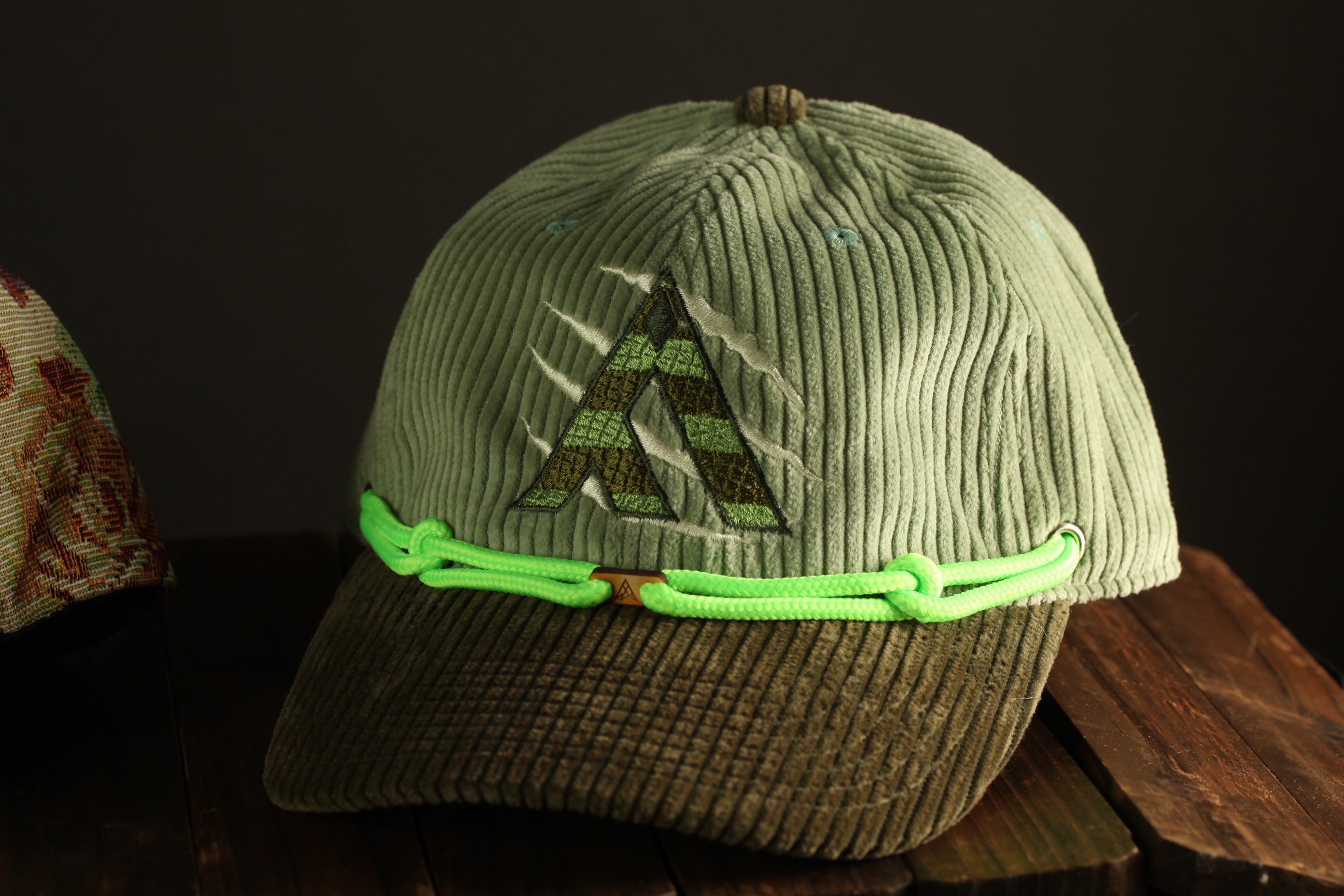 A worn green baseball cap with a distinctive logo on the front, resting on a wooden surface.