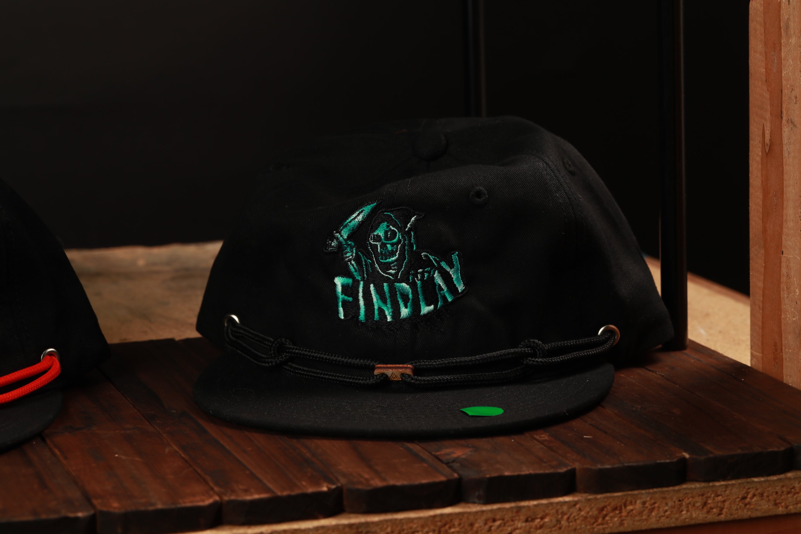 A black baseball cap with a skull and crossbones design and the word "FINDlay" printed on it, sitting on a wooden surface.