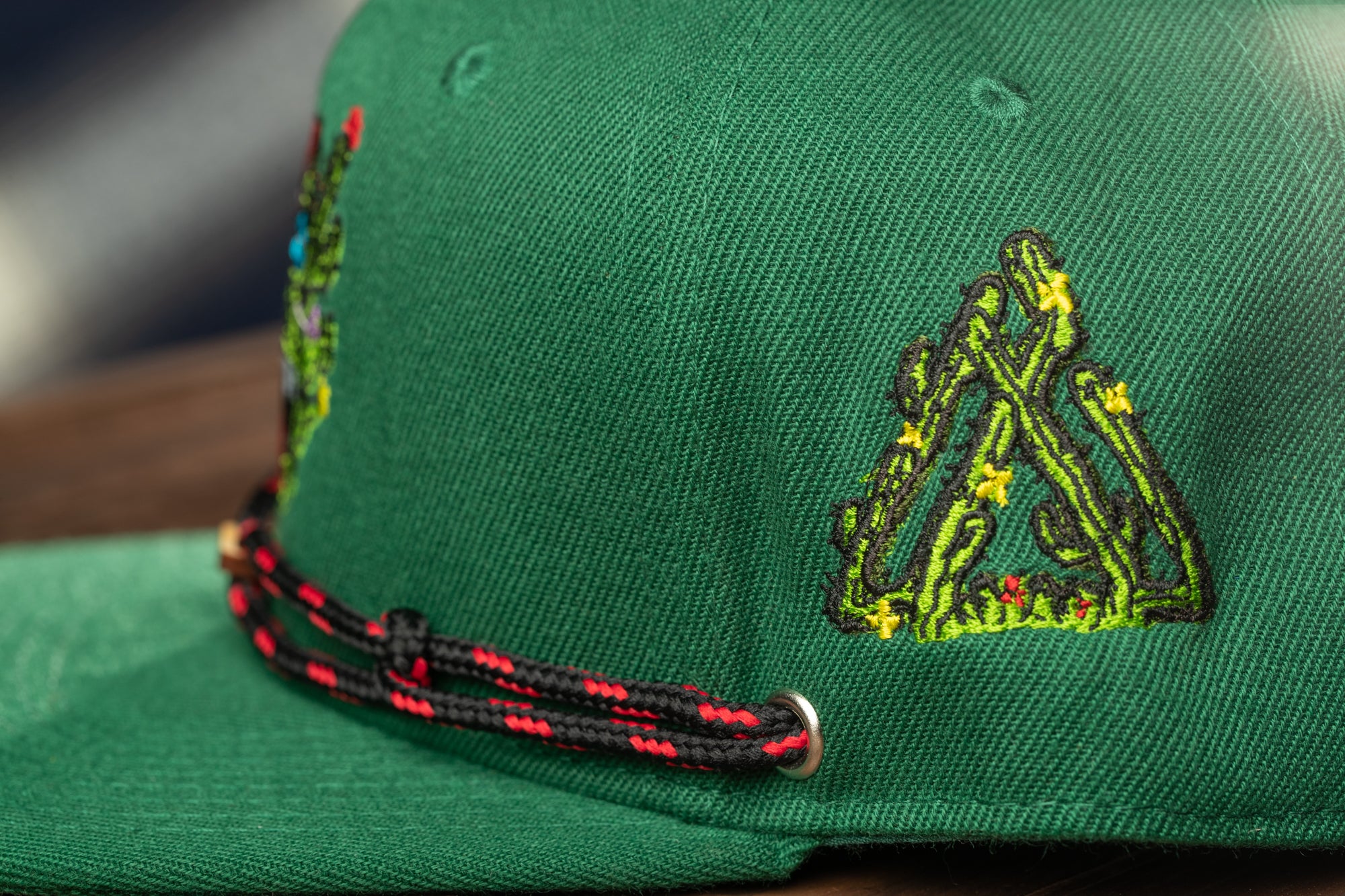 A close-up view of a green baseball cap with a red and black braided strap.