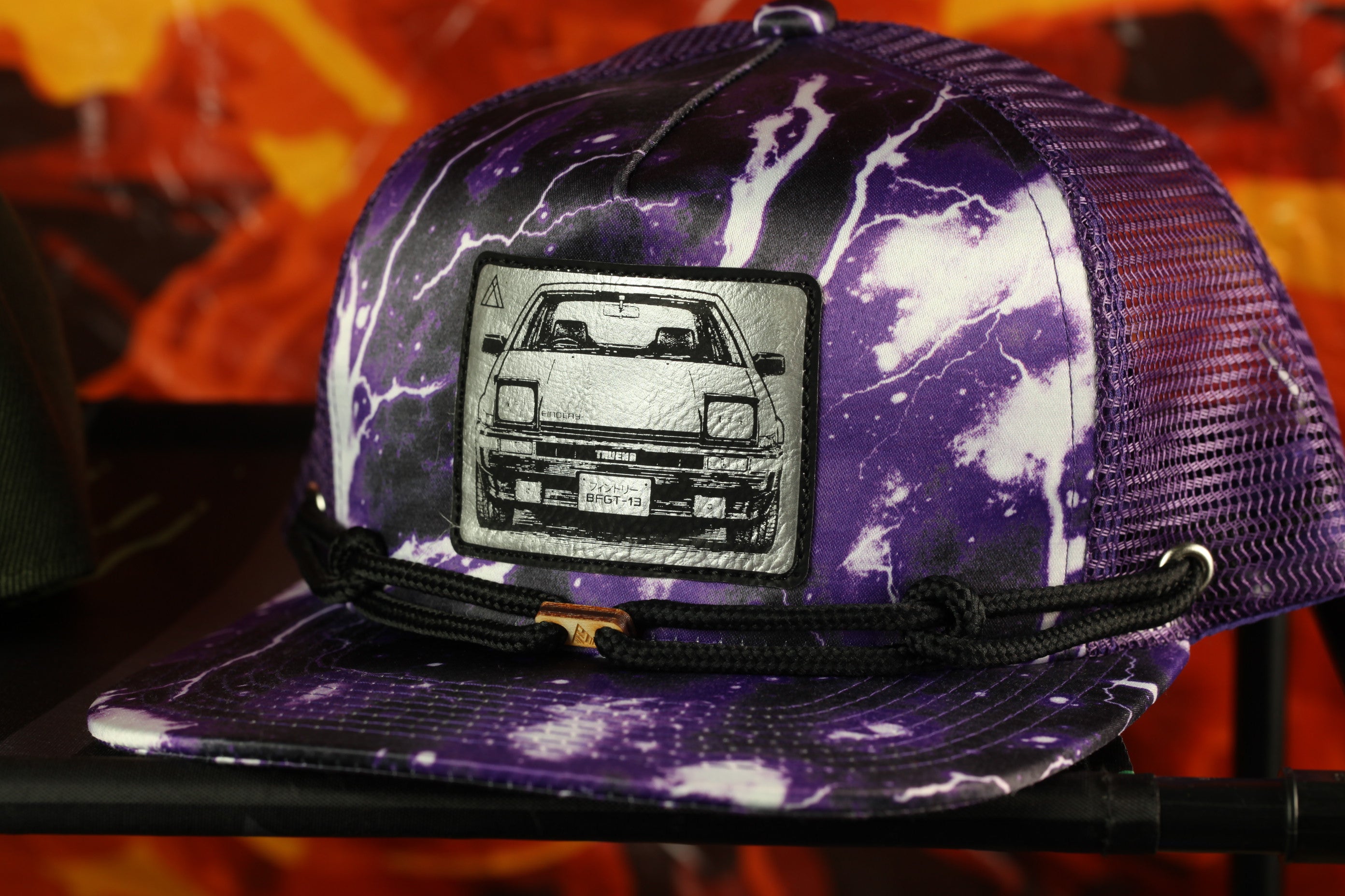 A purple baseball cap with a graphic of a car on the front, featuring a lightning bolt design.