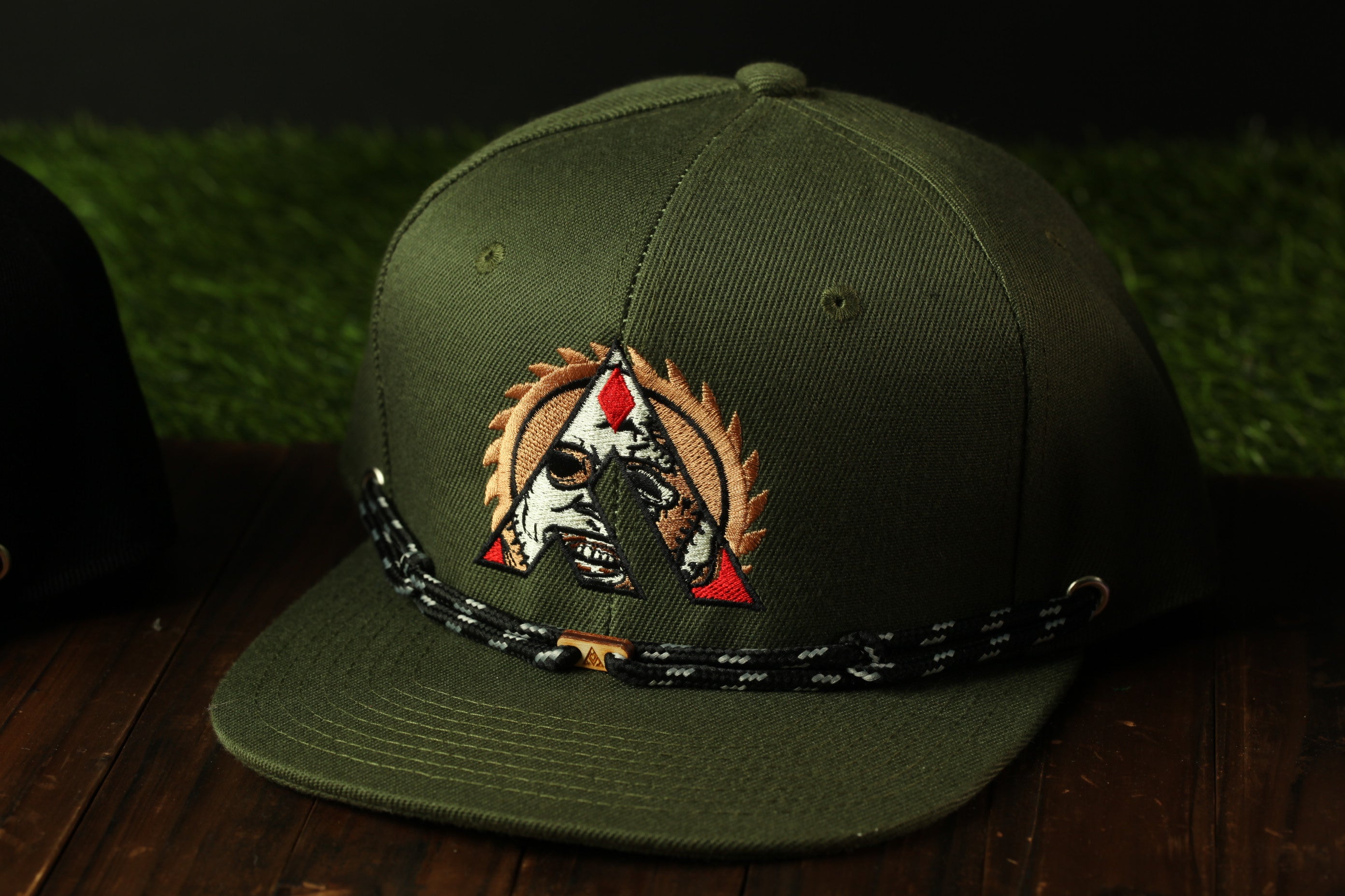 A dark green baseball cap with a distinctive logo on the front, placed on a wooden surface.