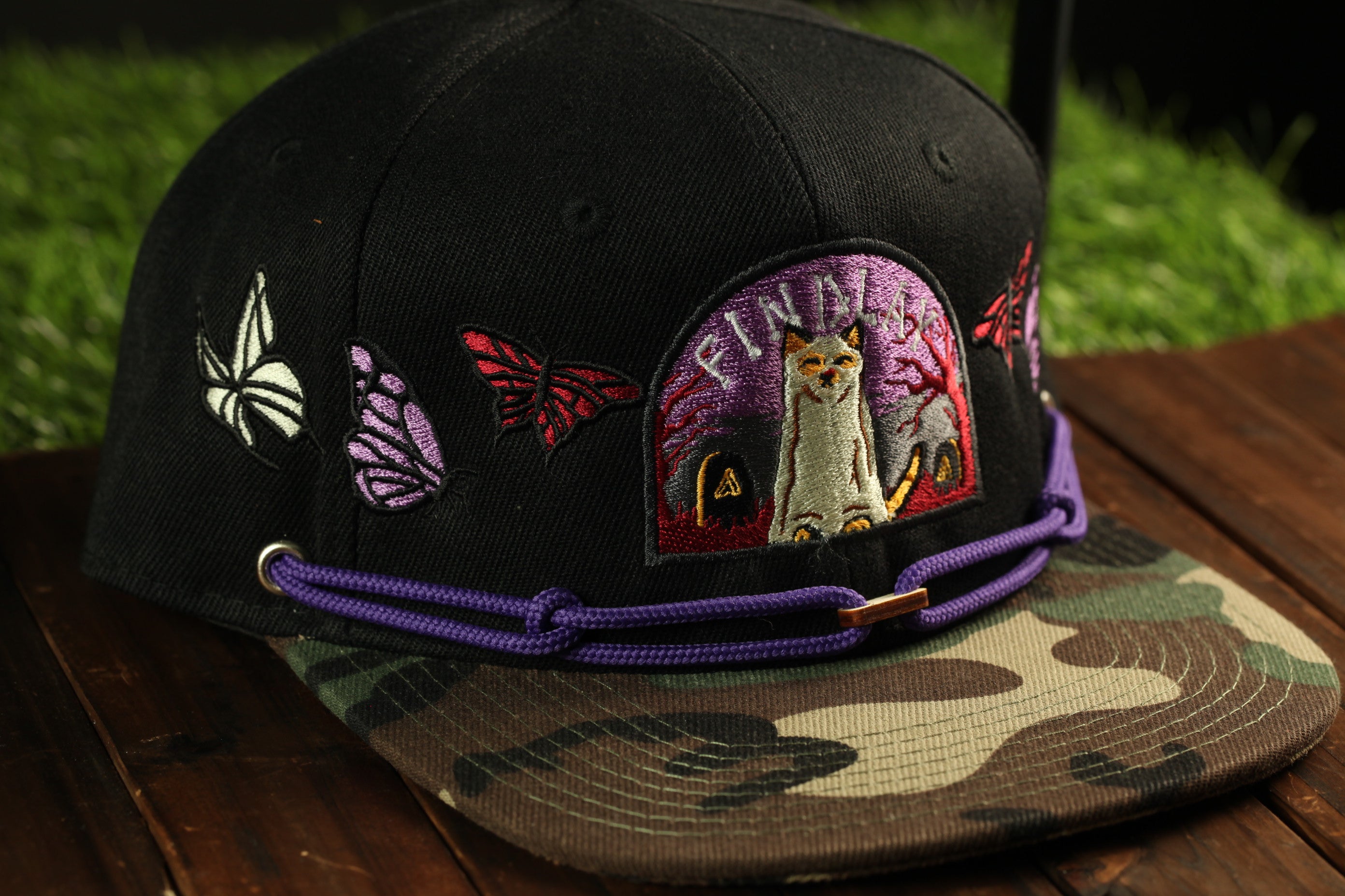 A black baseball cap with a camouflage pattern and colorful butterfly and owl embroidered designs on it.
