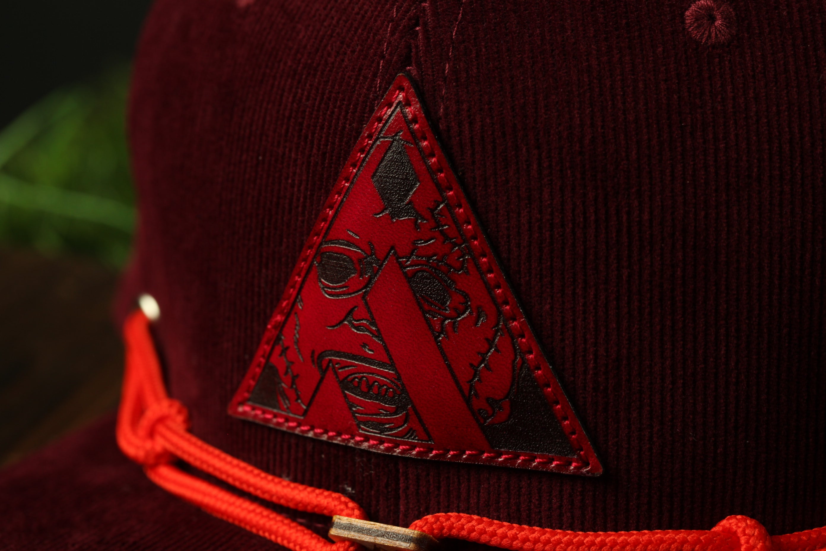A close-up view of a burgundy baseball cap with a red triangle-shaped logo on the front.