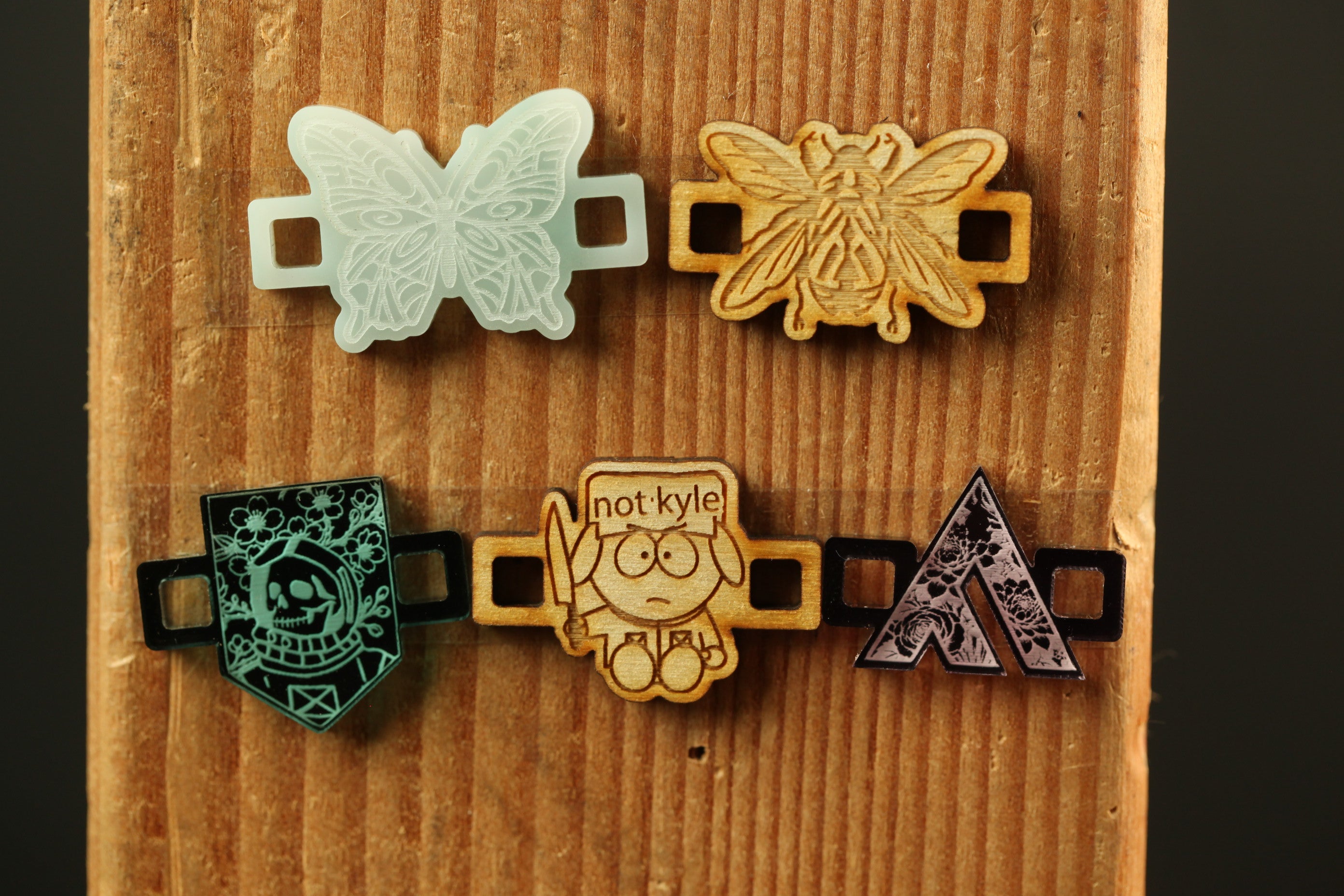 a wooden board with four different wooden objects attached to it, including a butterfly, a bee, a skull, and an arrow.