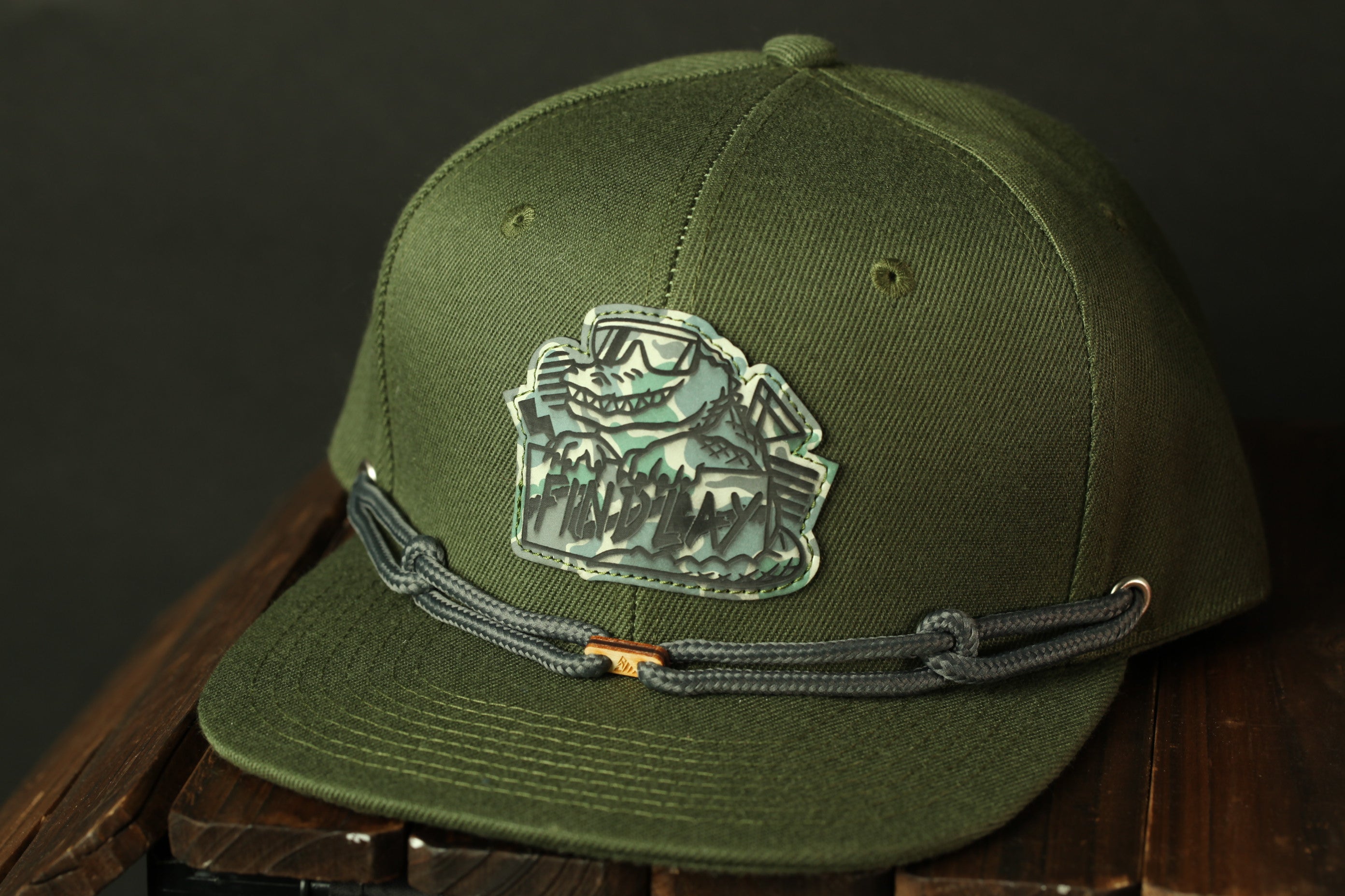 A green baseball cap with a graphic patch on the front, sitting on a wooden surface.
