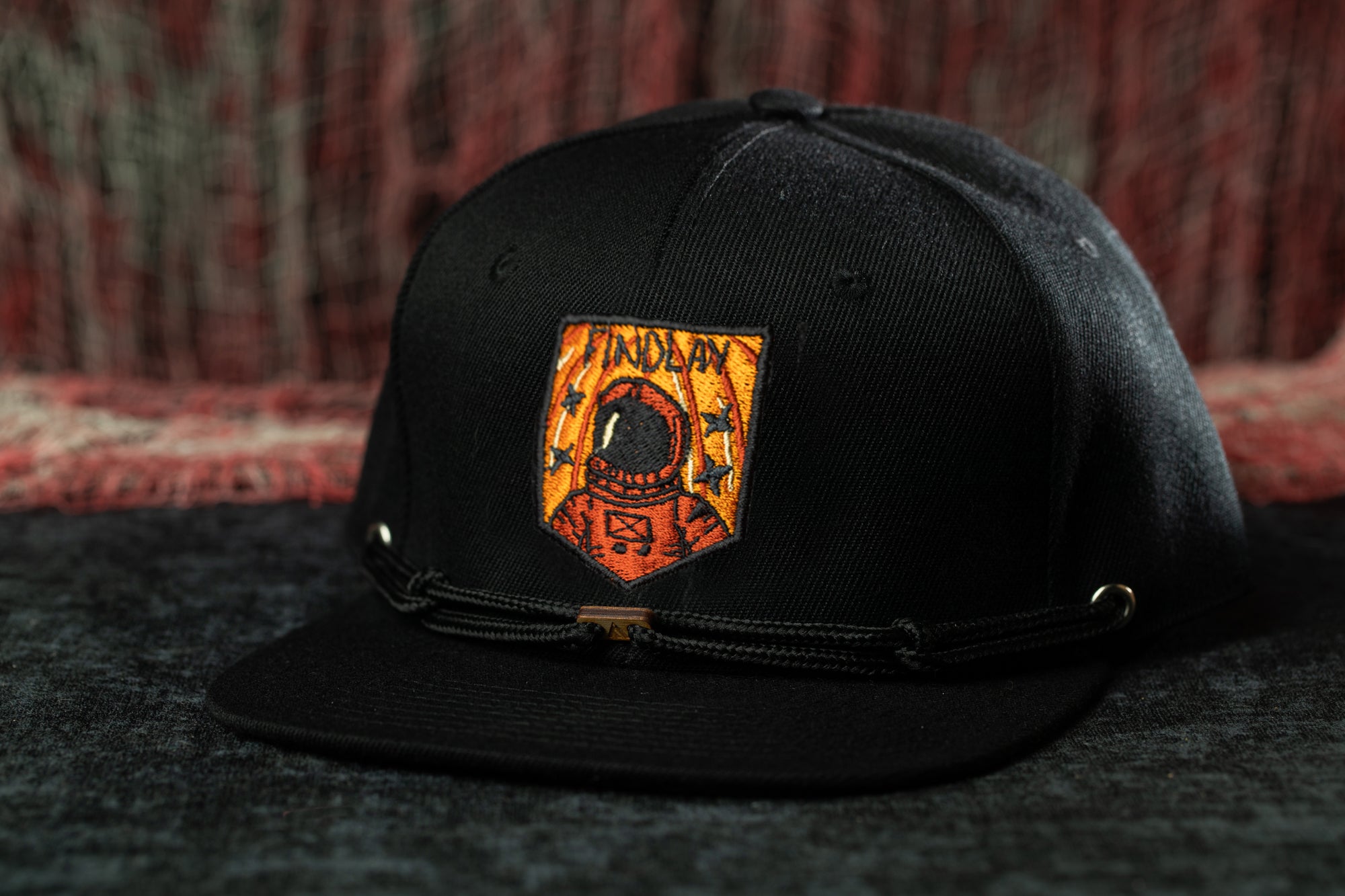 A black baseball cap with an orange and black patch featuring an astronaut design.