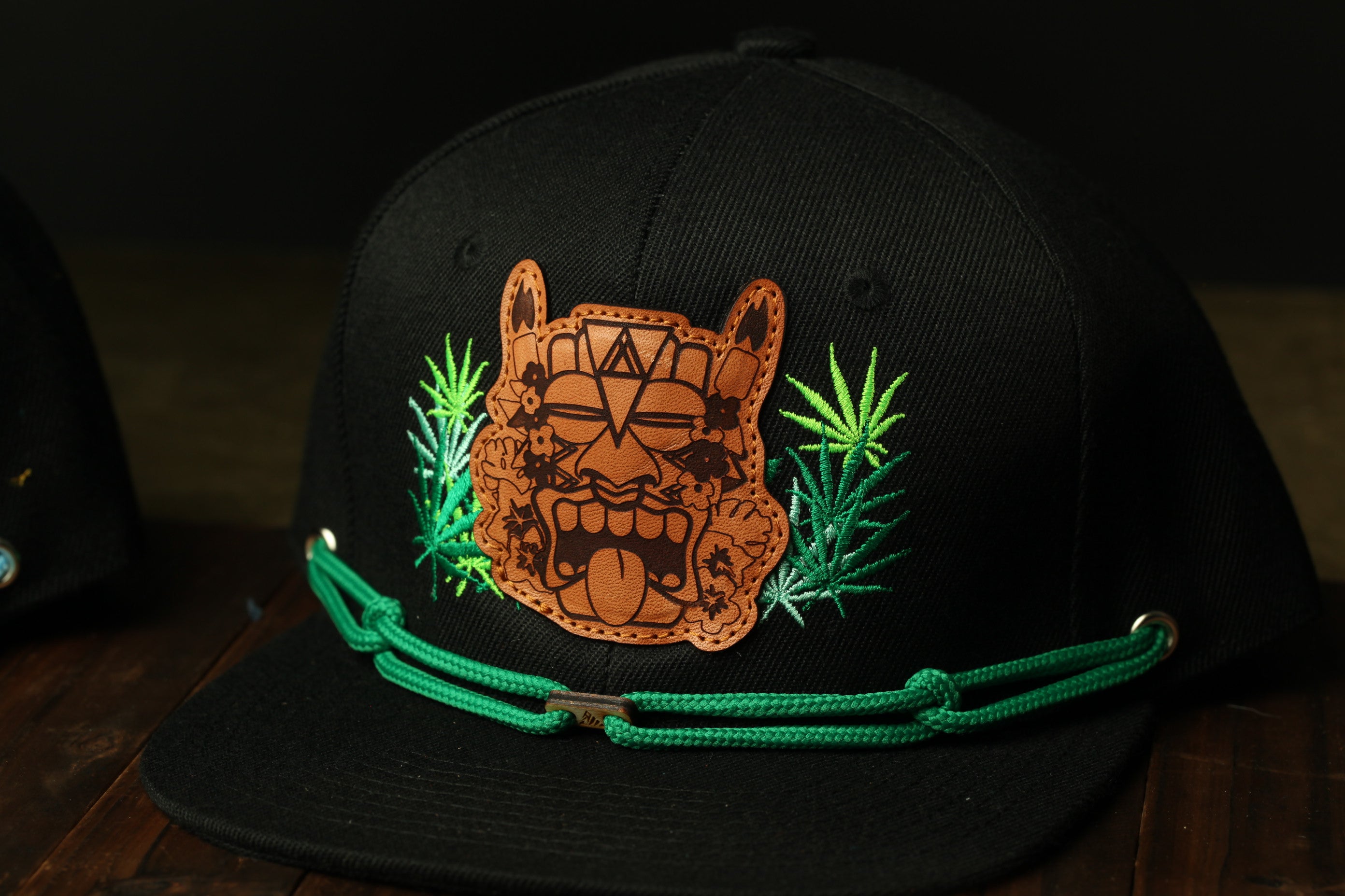 A black baseball cap with a brown embroidered face and green strings.