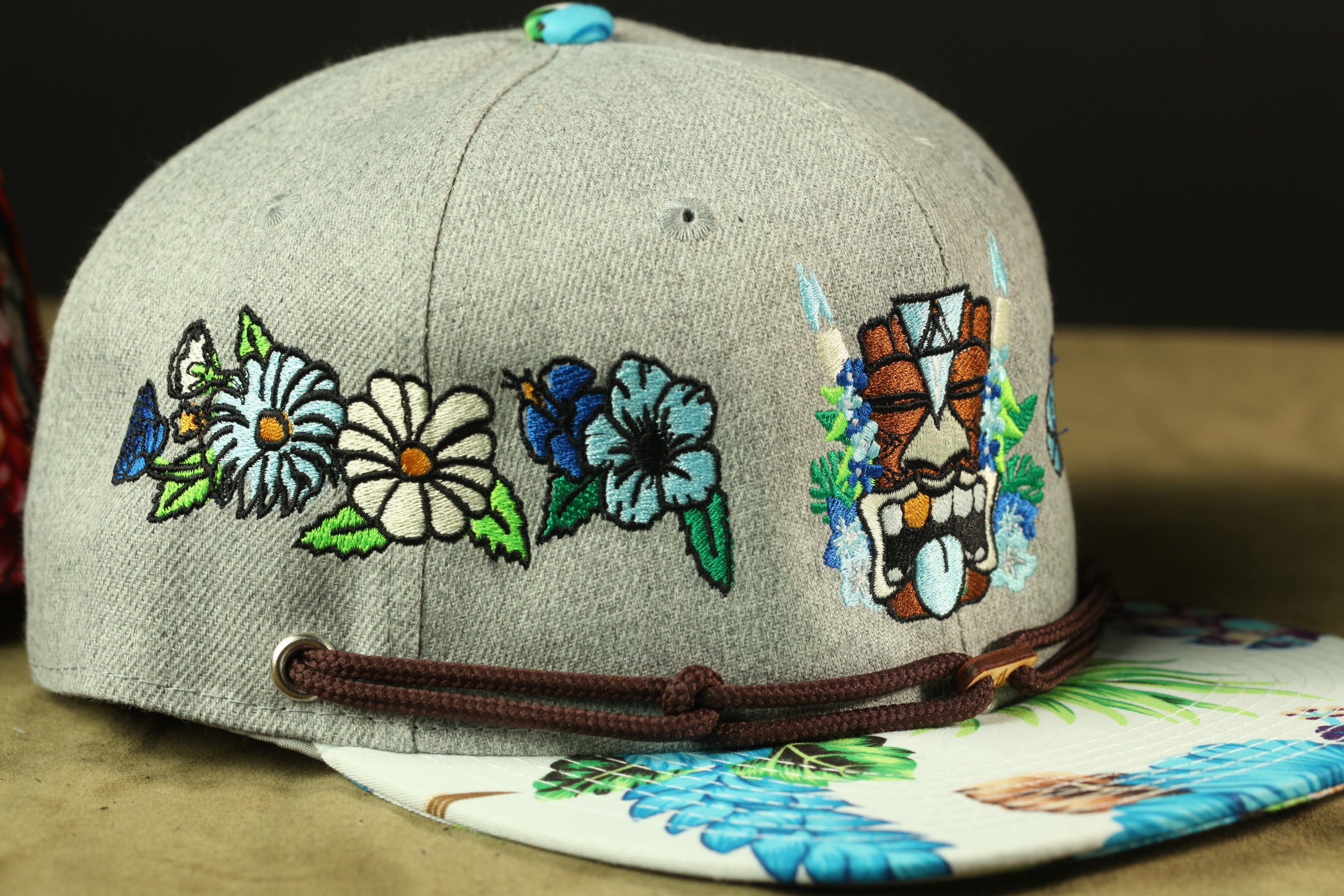 A gray baseball cap with colorful floral and tiki-style embroidered designs on the front.