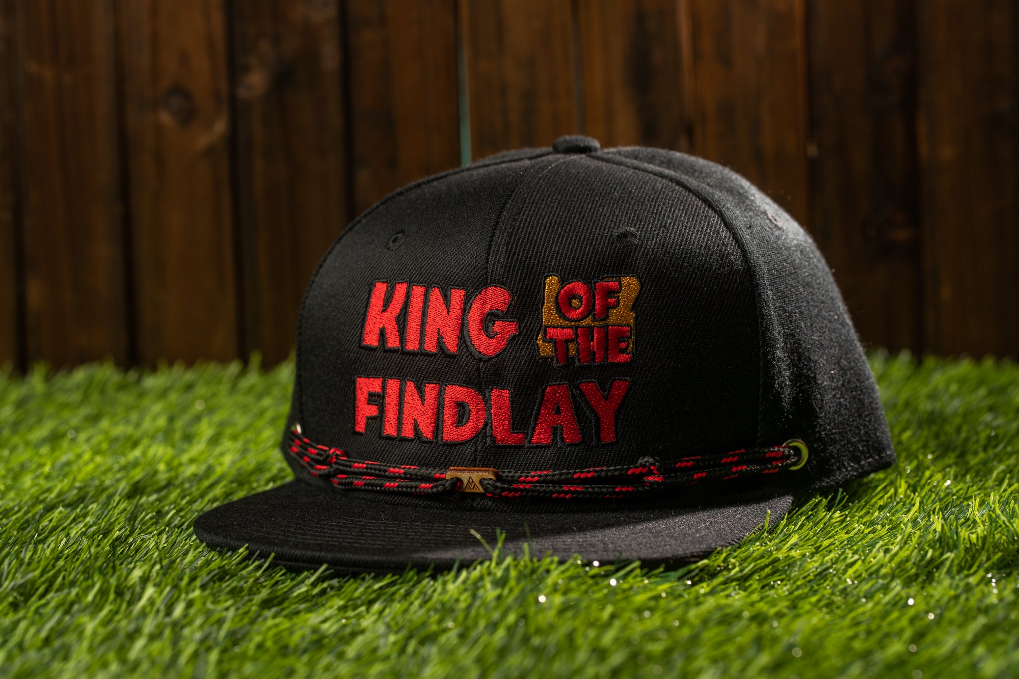 A black baseball cap with red text on it, sitting on a grassy surface.